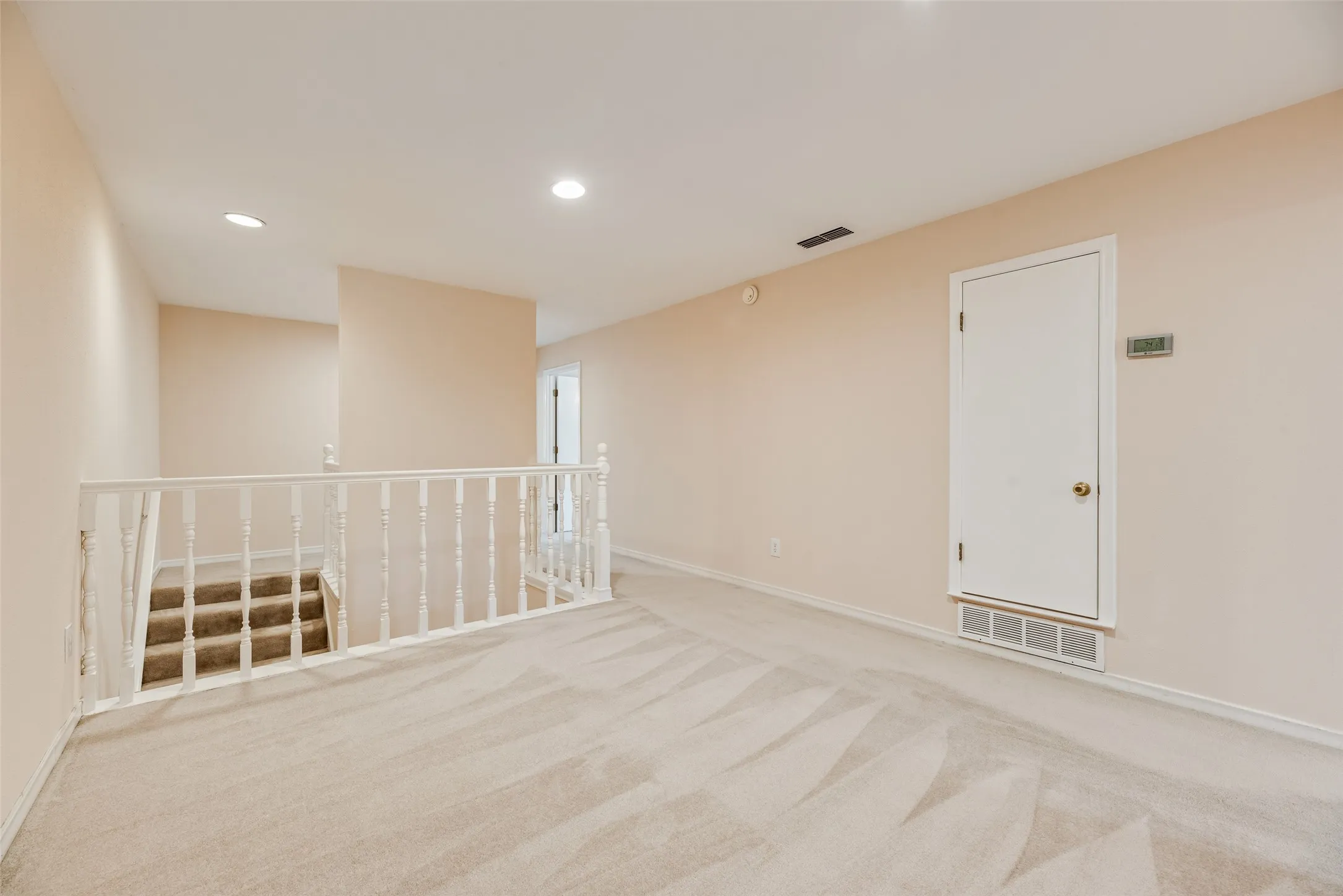 Carpeted landing featuring a white painted baluster railing, recessed lighting, and a neutral wall color