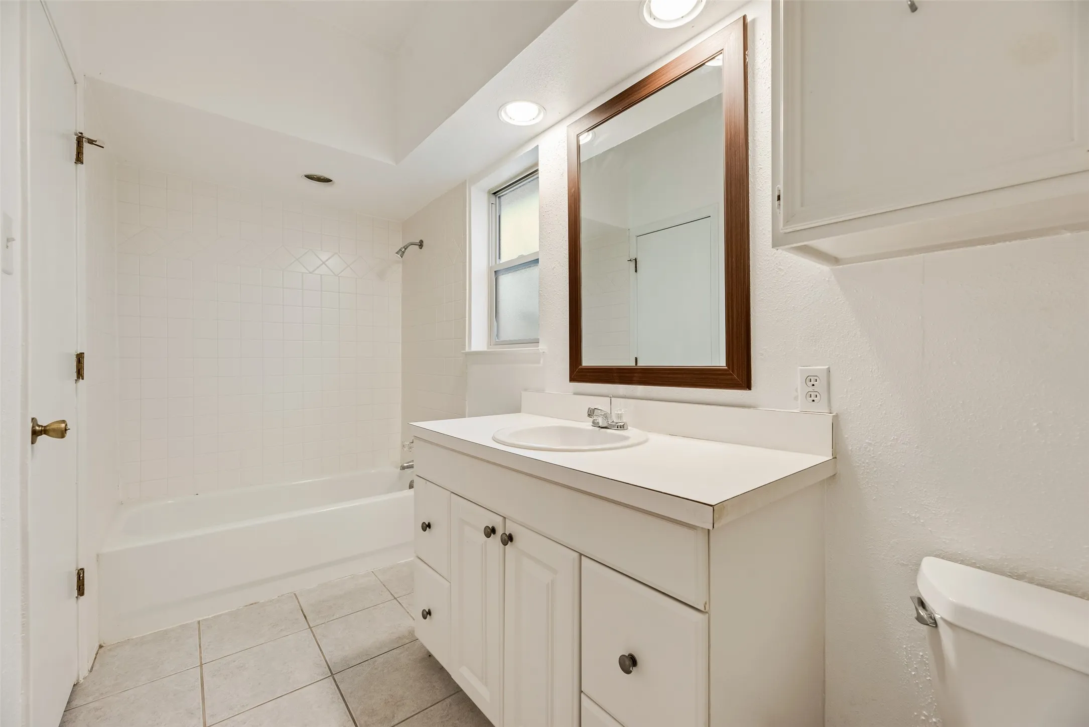 Bathroom featuring a white vanity with integrated sink, a rectangular framed mirror, an overhead recessed light, and a window for natural light