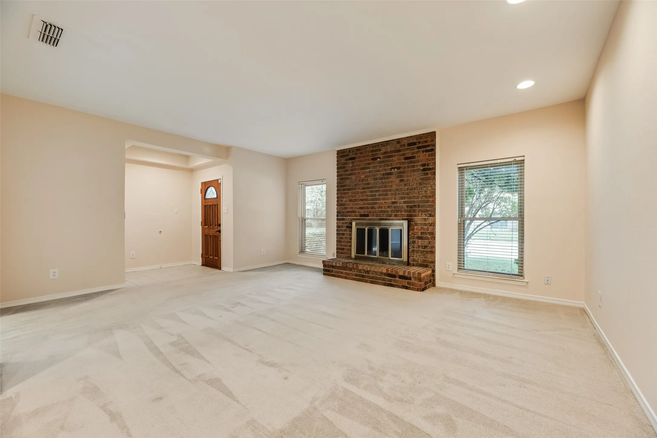 Spacious room featuring a brick fireplace, neutral carpet, and recessed lighting