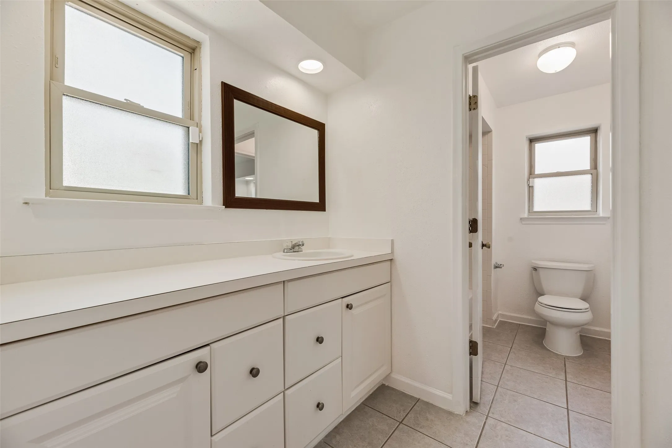 Bathroom featuring a white vanity with integrated sink, a framed wall mirror, and two windows with frosted glass