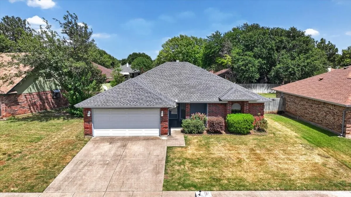 Traditional brick exterior featuring a grey shingle roof, attached two-car garage, concrete driveway, and mature landscaping