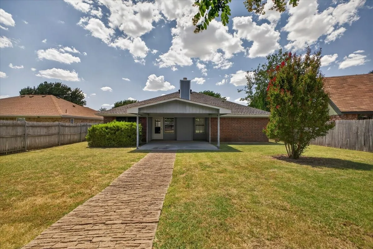 Expansive backyard featuring a stone-look paver walkway, mature trees, and a covered patio area