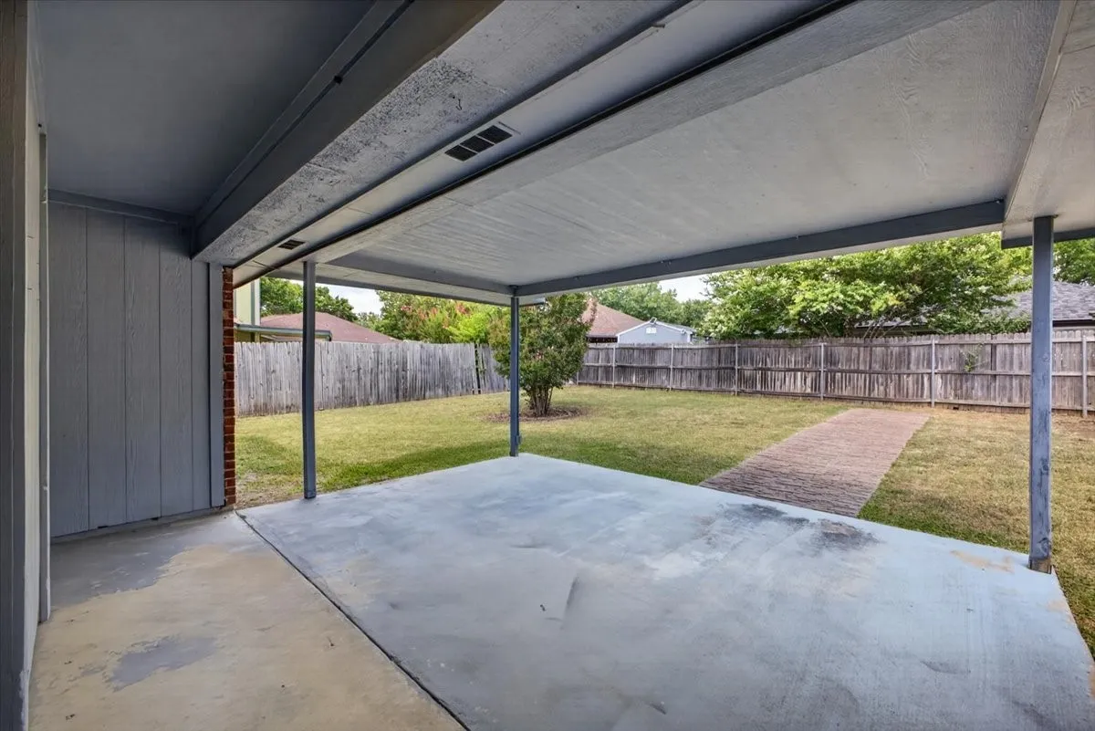 Covered concrete patio with metal support columns and a privacy fence enclosing the backyard