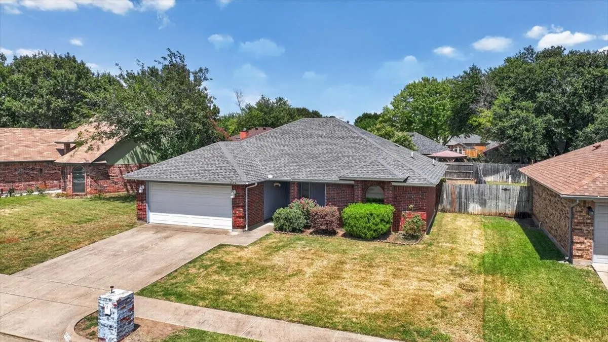 Brick exterior residence featuring a grey shingle roof, attached garage, and concrete driveway