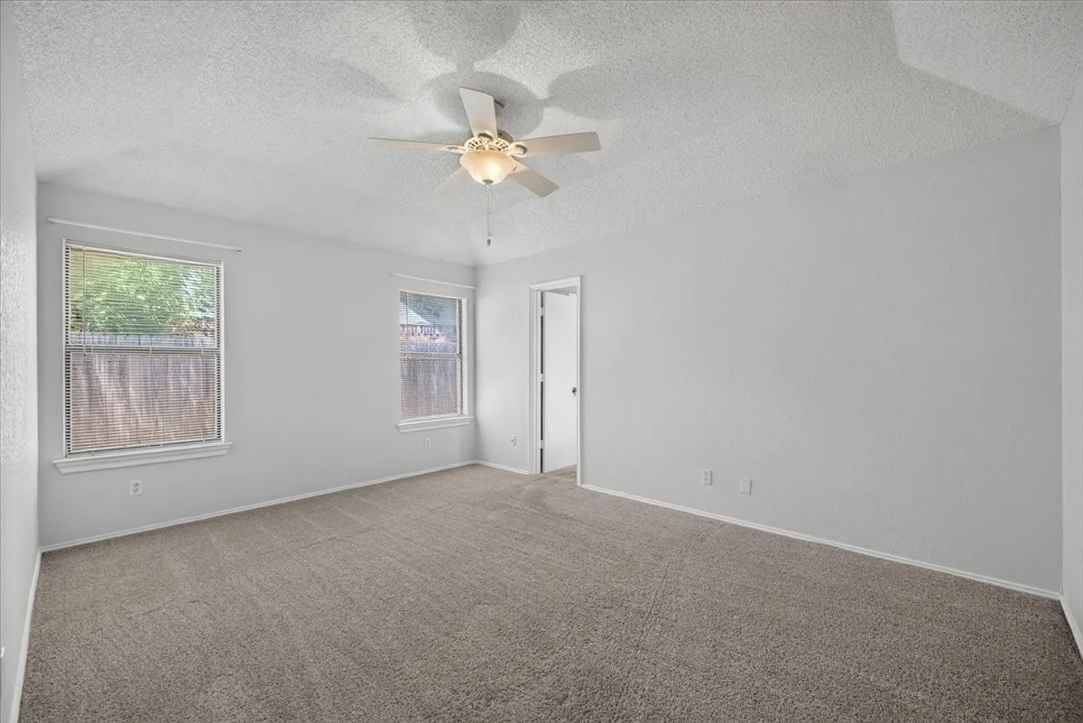 Spacious carpeted room featuring a ceiling fan with integrated lighting, two windows, and light-toned walls