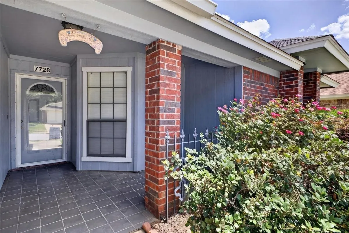 Entryway featuring brick accents, a gray tiled porch, a gray front door with decorative glass, a prominent bay window, and exterior lighting