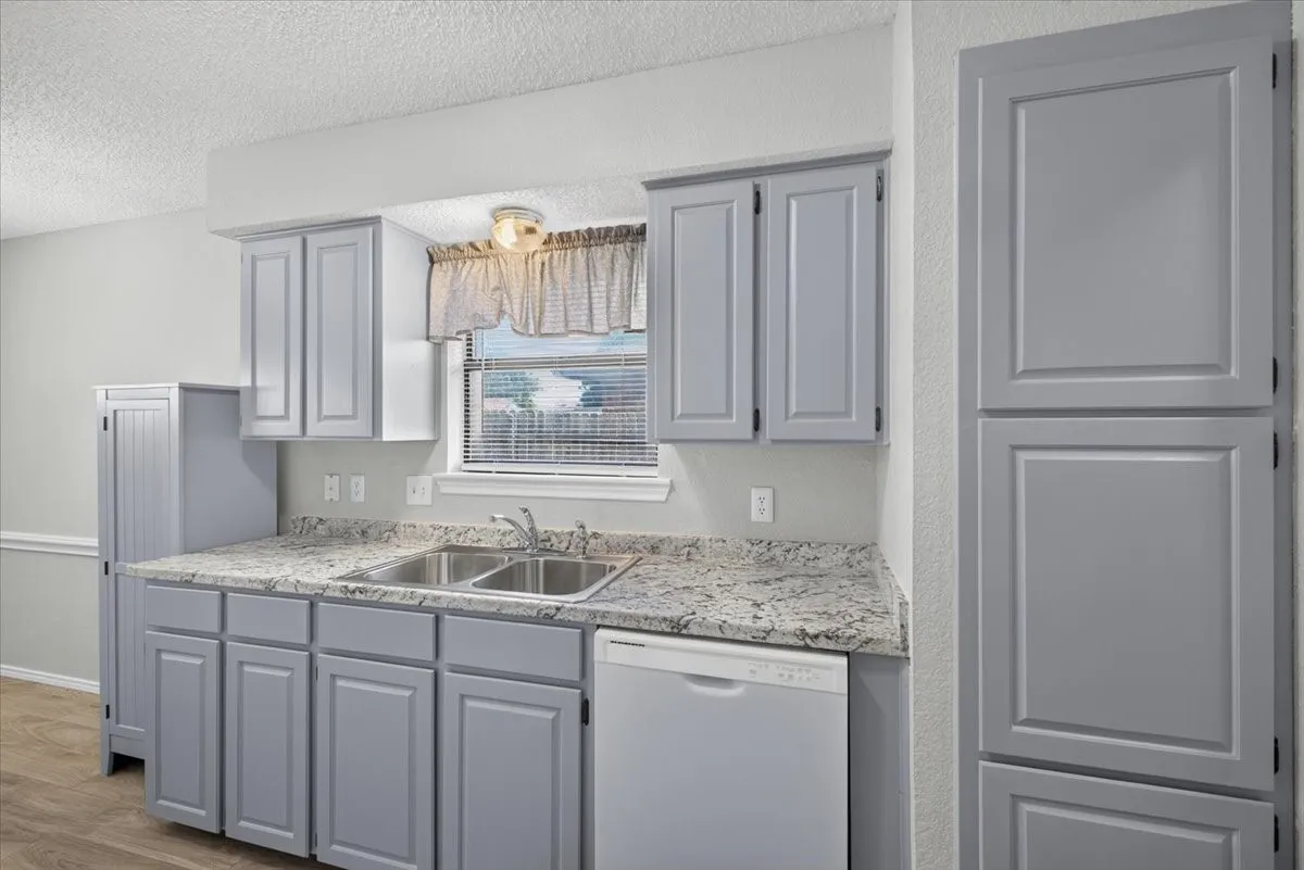 Kitchen featuring light gray shaker-style cabinetry, granite-look countertops, a double basin stainless steel sink, and a built-in dishwasher