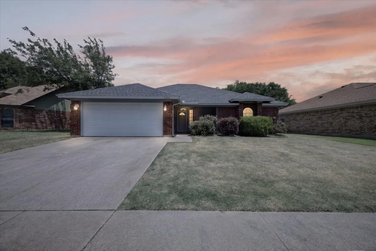 Brick facade residence featuring a two-car garage, concrete driveway, and mature front landscaping