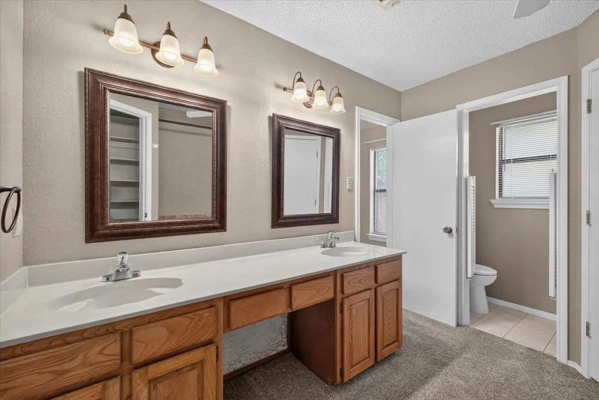 Bathroom featuring a dual vanity with light wood cabinetry, white countertops, and two framed mirrors