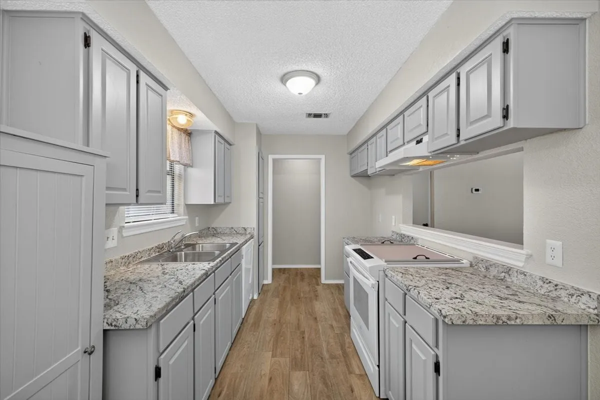 Galley kitchen featuring light gray cabinetry, wood-finish flooring, and light-toned countertops