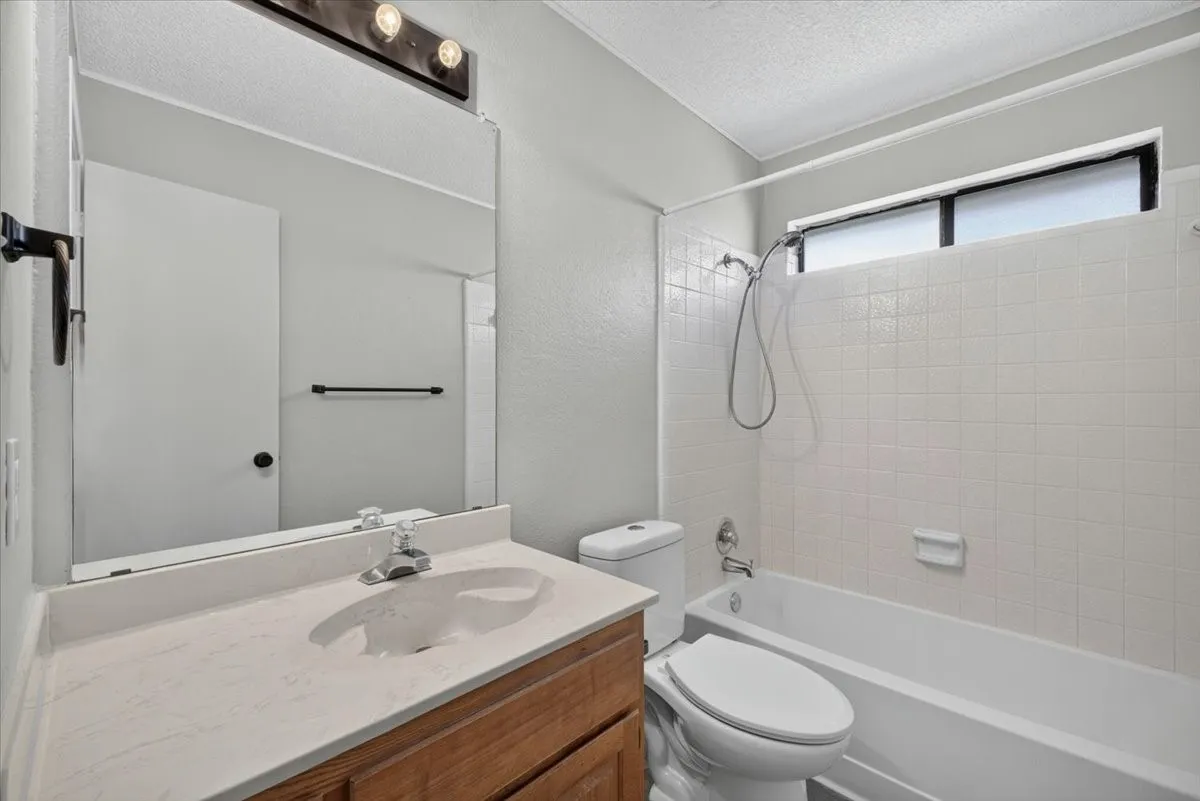 Bathroom featuring a wood-finish vanity with an integrated sink and light-toned countertop, a frameless mirror, and a three-light vanity fixture