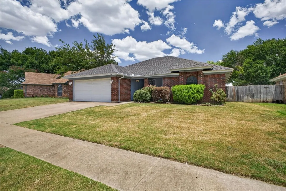 Brick exterior residence with an attached garage, a paved driveway, and established landscaping
