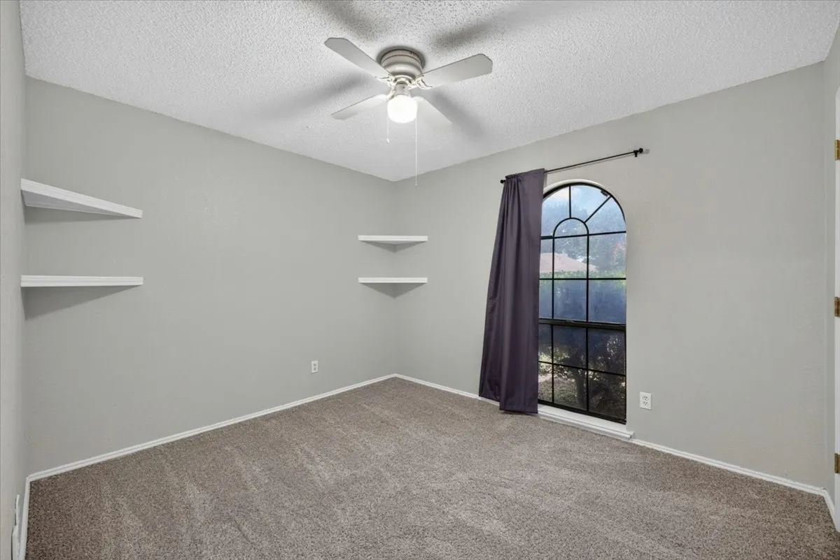 Carpeted room featuring an arched window, ceiling fan, and built-in floating shelves