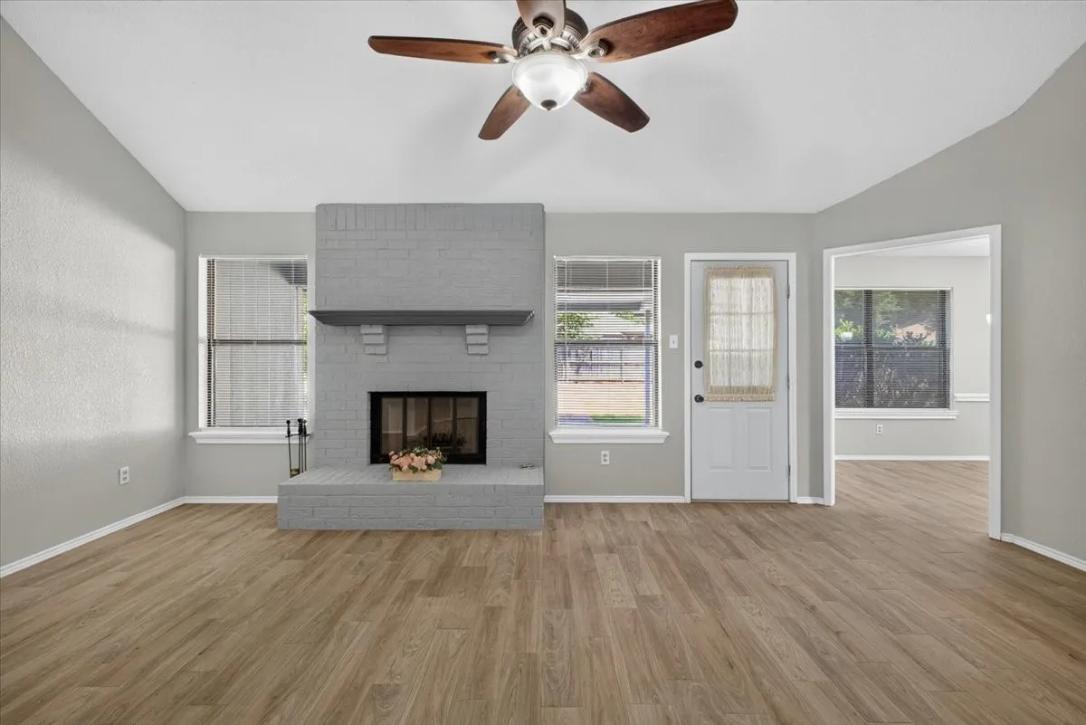 Living area featuring a painted brick fireplace with a mantel, wood-finish flooring, a ceiling fan, and multiple windows for natural light