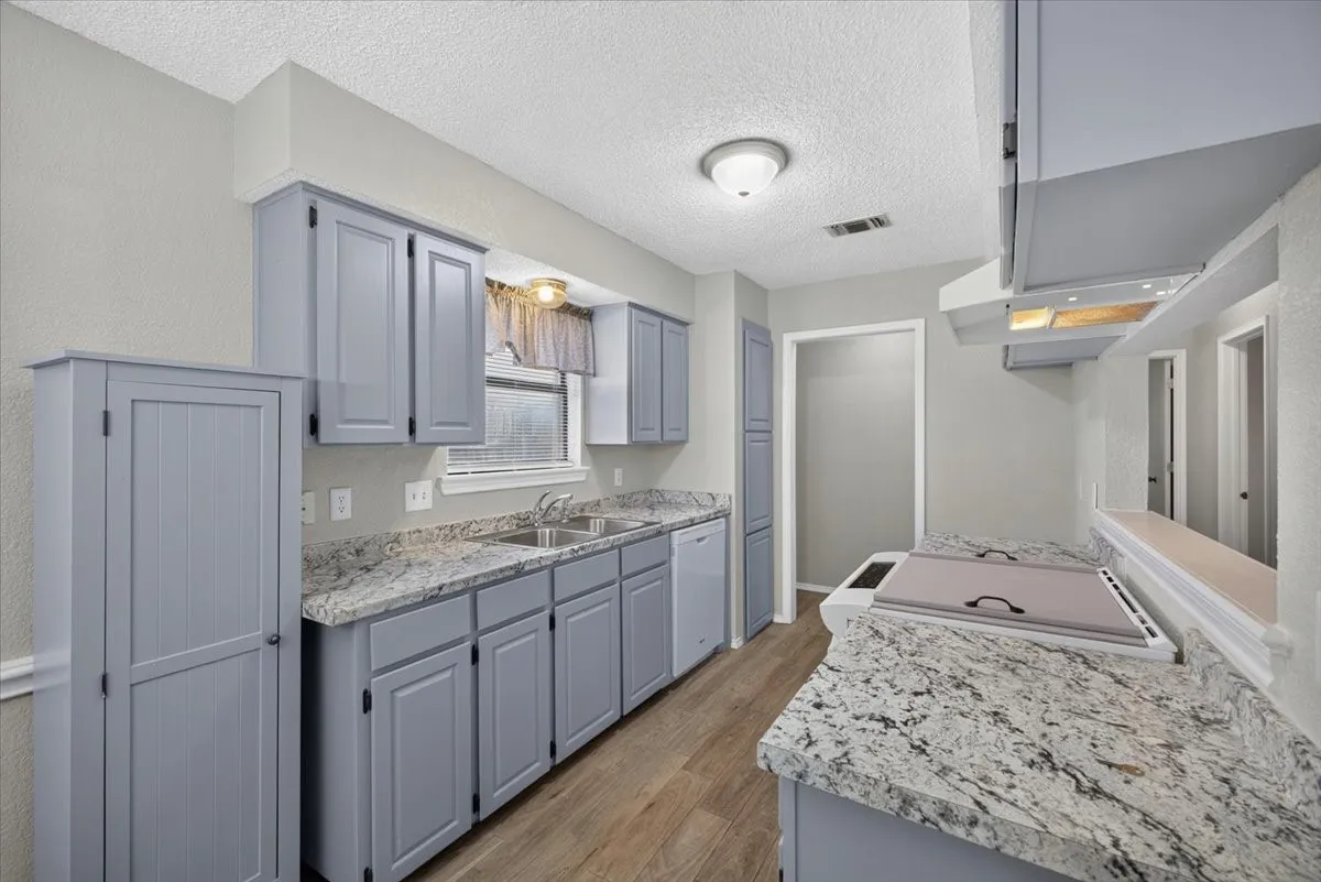 Kitchen featuring extensive stone-finish countertops, light gray cabinetry, wood-finish flooring, a double basin sink, and a built-in electric cooktop