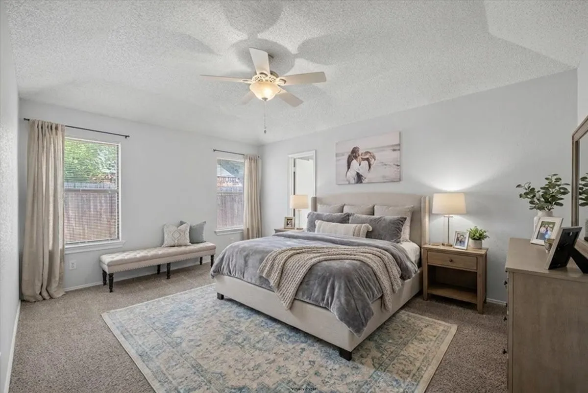Spacious bedroom featuring neutral wall tones, carpet flooring, a ceiling fan with integrated lighting, and two large windows
