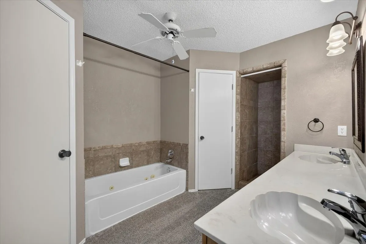 Bathroom featuring a dual vanity with shell-shaped sinks, a walk-in shower with tile surround, a jetted bathtub with a partial tile surround, and a ceiling fan