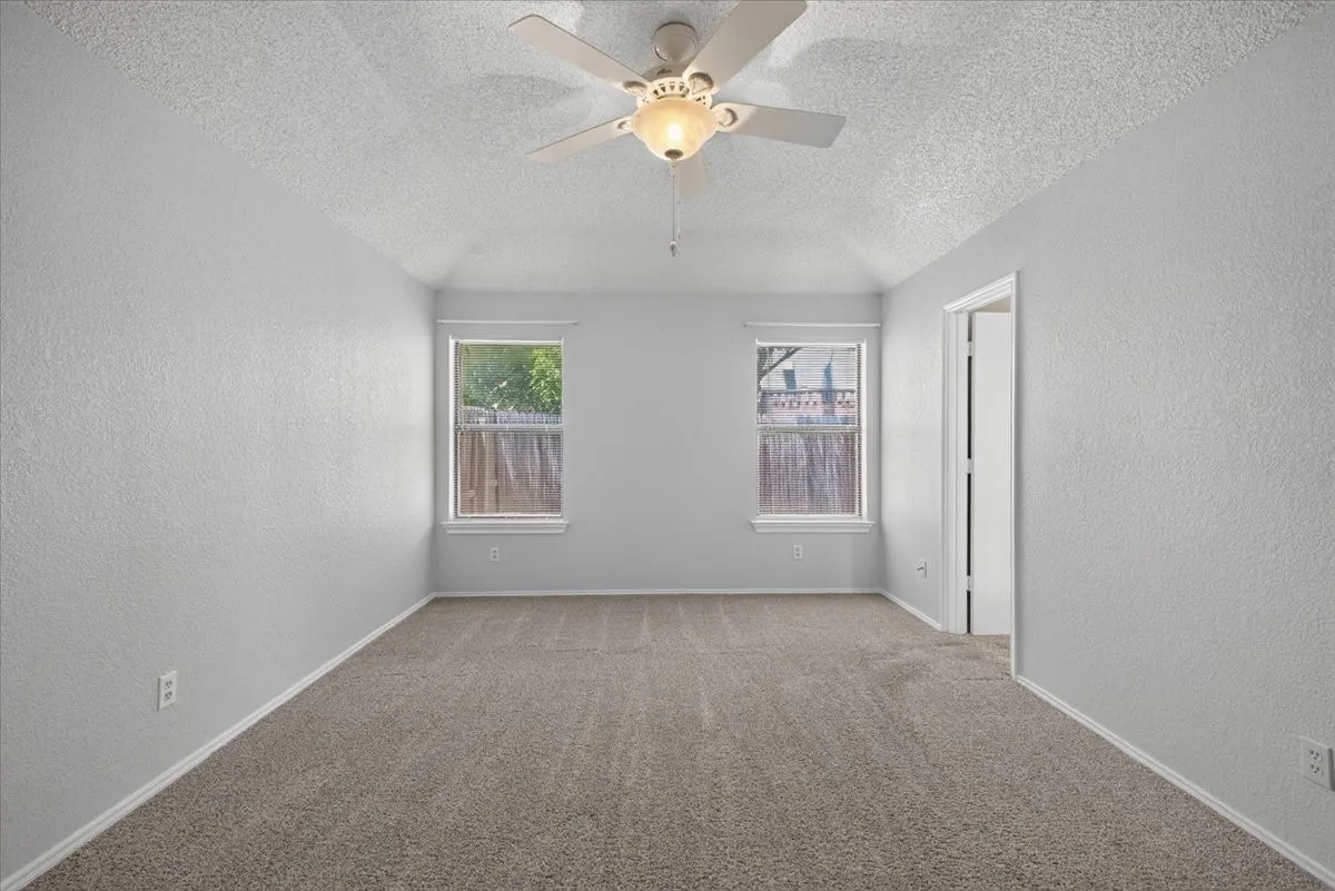Spacious room featuring vaulted ceilings, light gray textured walls, and a neutral carpeted floor