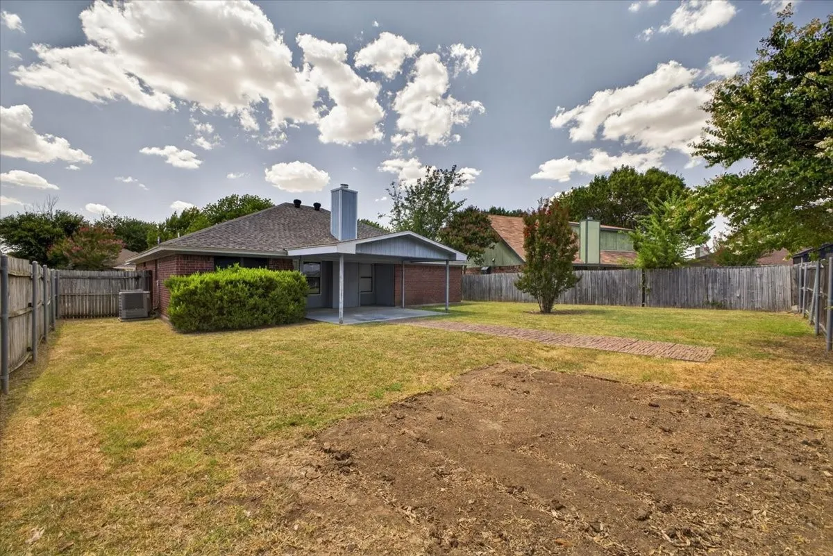 Expansive backyard featuring a covered patio, brick exterior, wood fence, mature trees, and a dedicated garden area