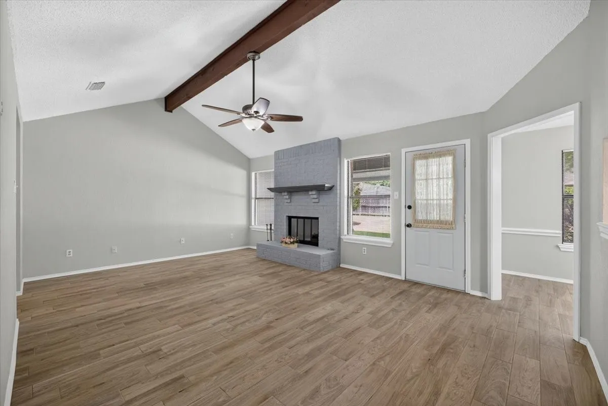 Living area featuring a vaulted ceiling with an exposed wood beam, a ceiling fan, and wood-finish flooring
