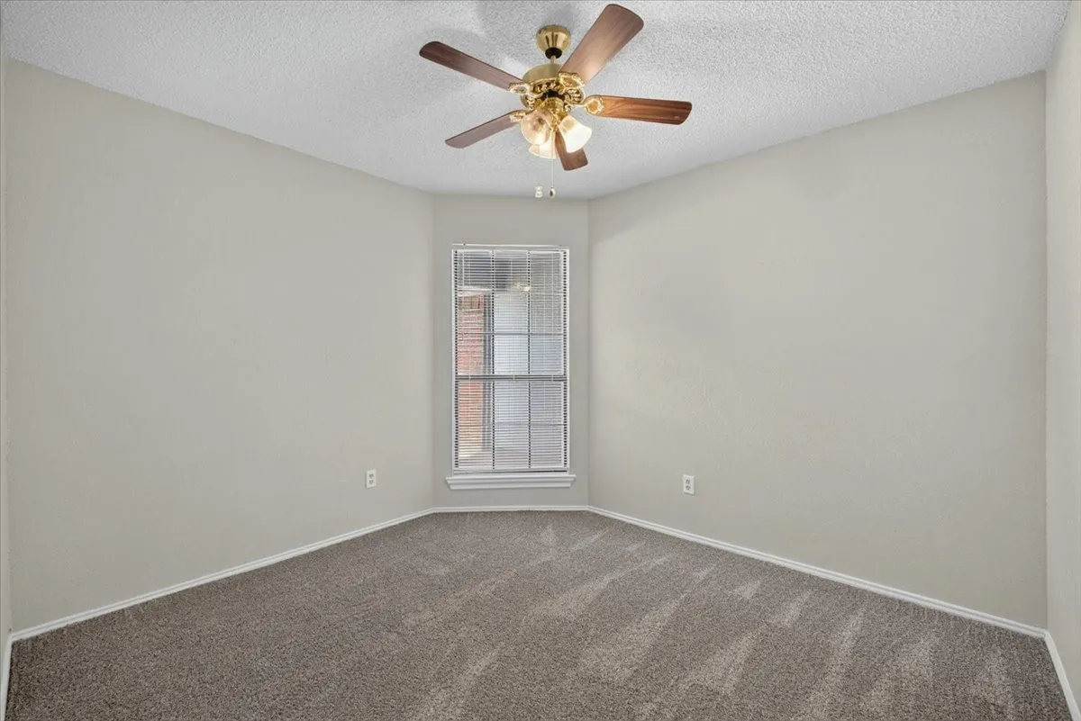 Carpeted room with a bay window, ceiling fan with light fixture, and neutral painted walls