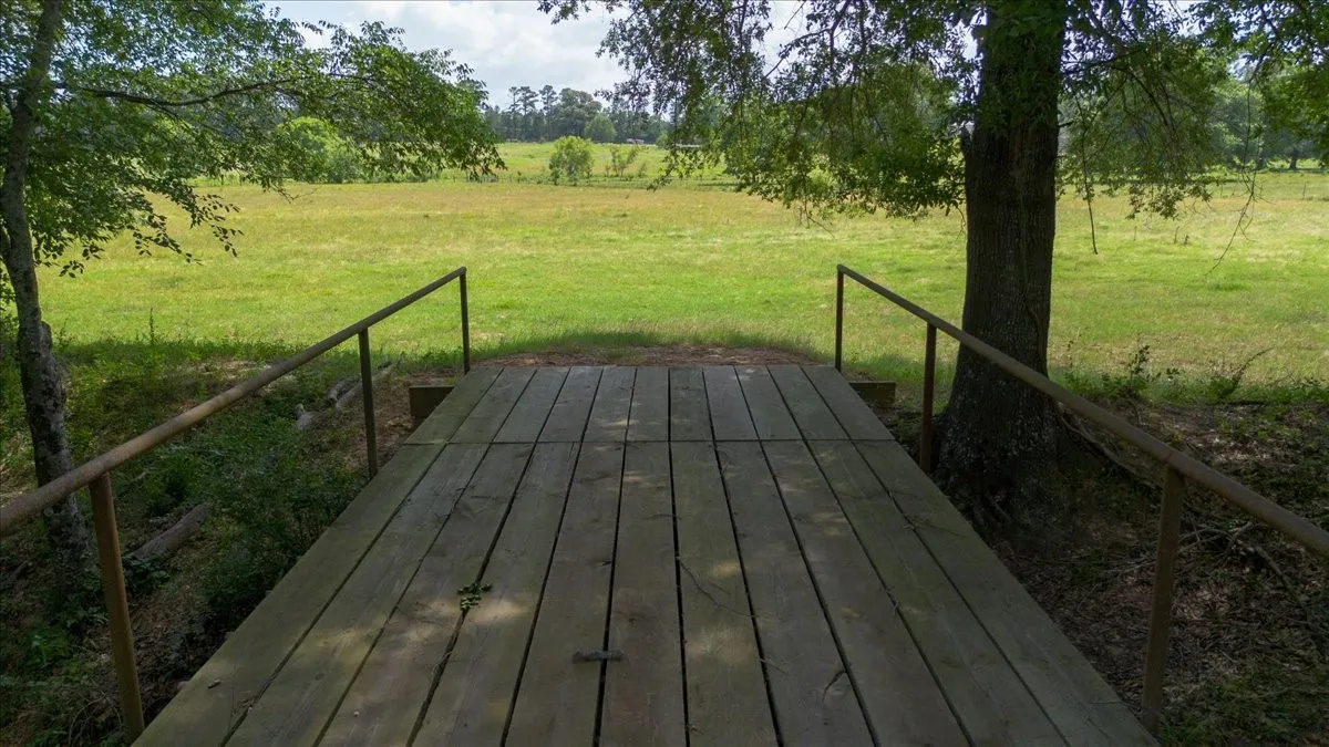 Wood-plank bridge with metal handrails, surrounded by mature trees and verdant fields