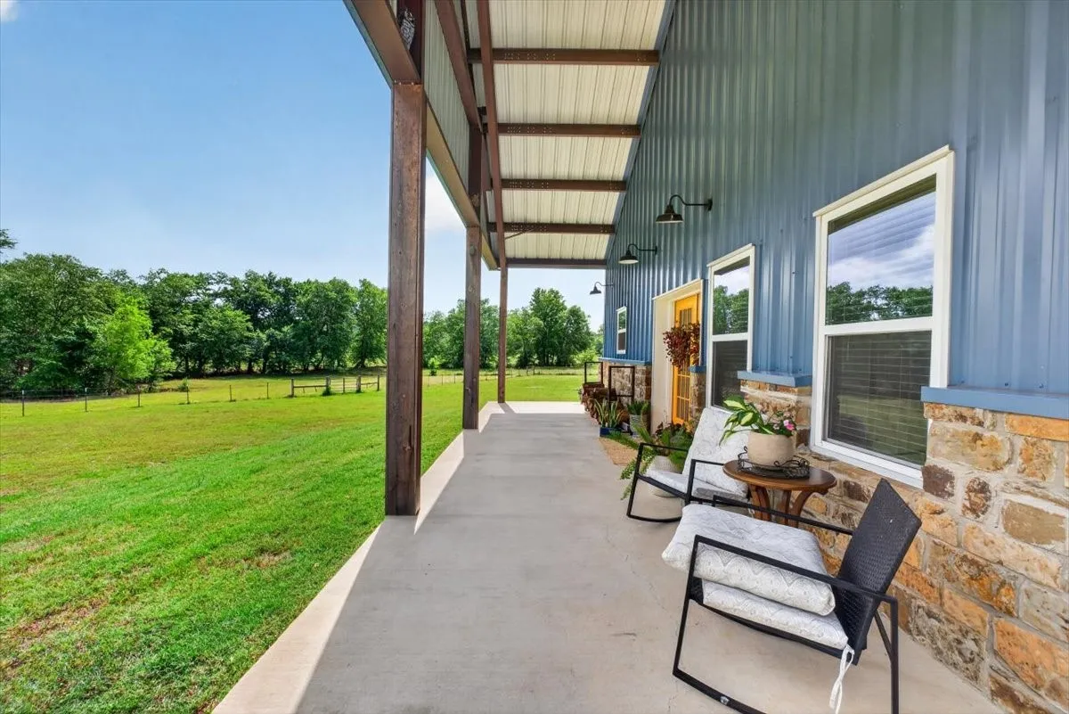 Expansive covered porch featuring a concrete slab, exposed structural beams, and barn-style lighting fixtures