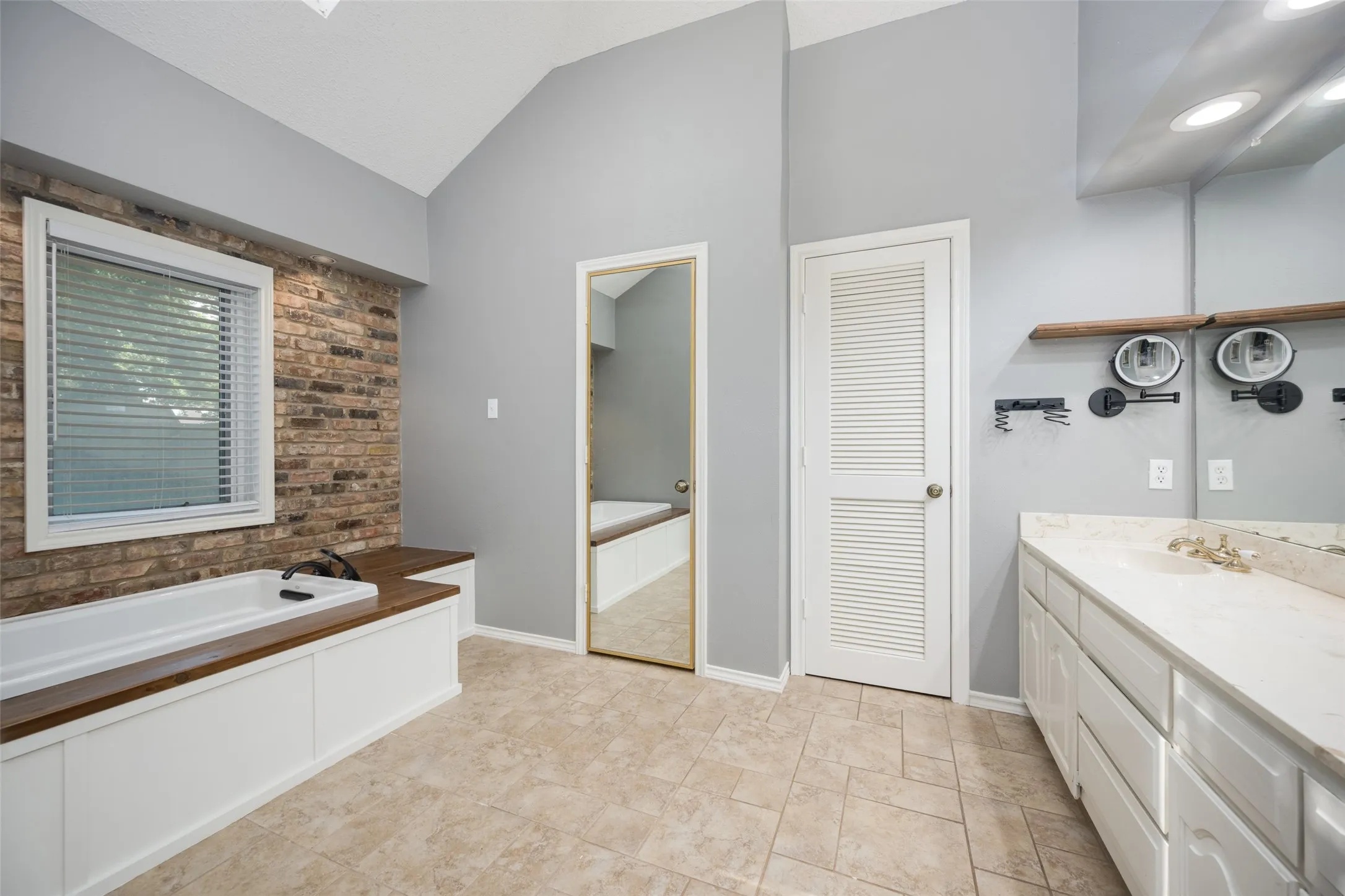 Bathroom featuring a soaking tub with wood-finish surround, a brick accent wall, and vaulted ceilings