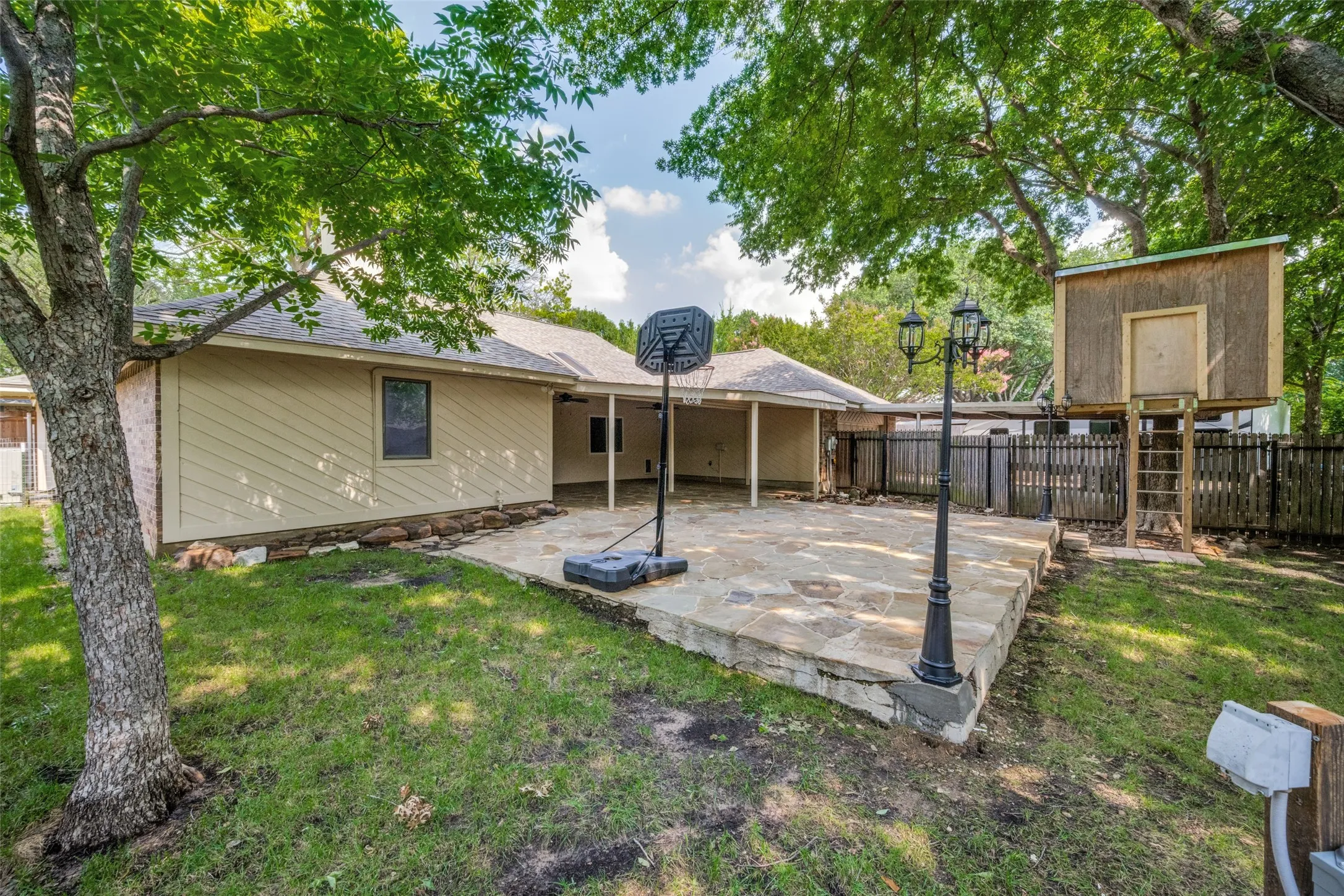 Expansive flagstone patio area with a covered extension, surrounded by mature trees