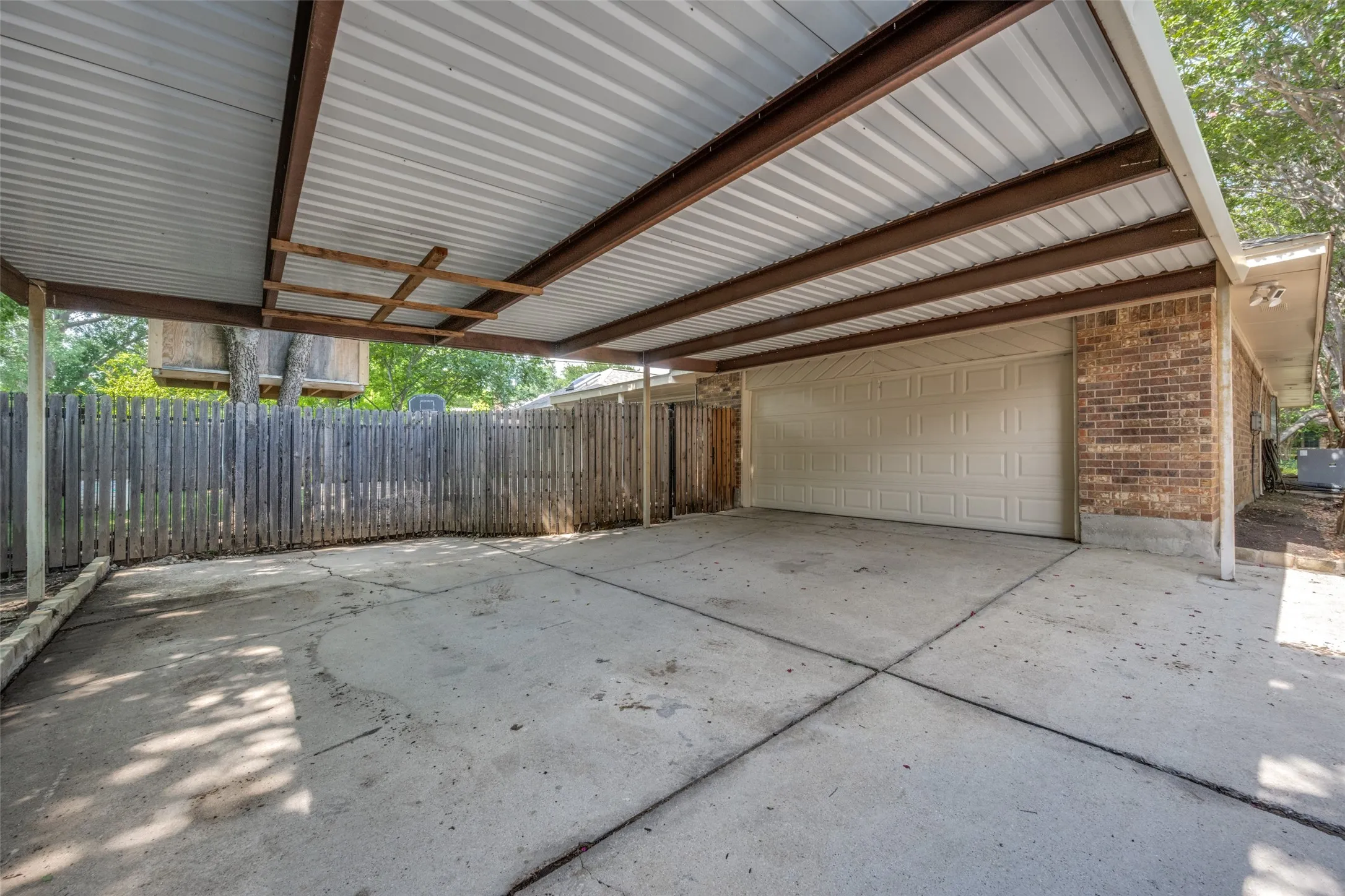 Concrete driveway featuring a metal carport structure with exposed beams