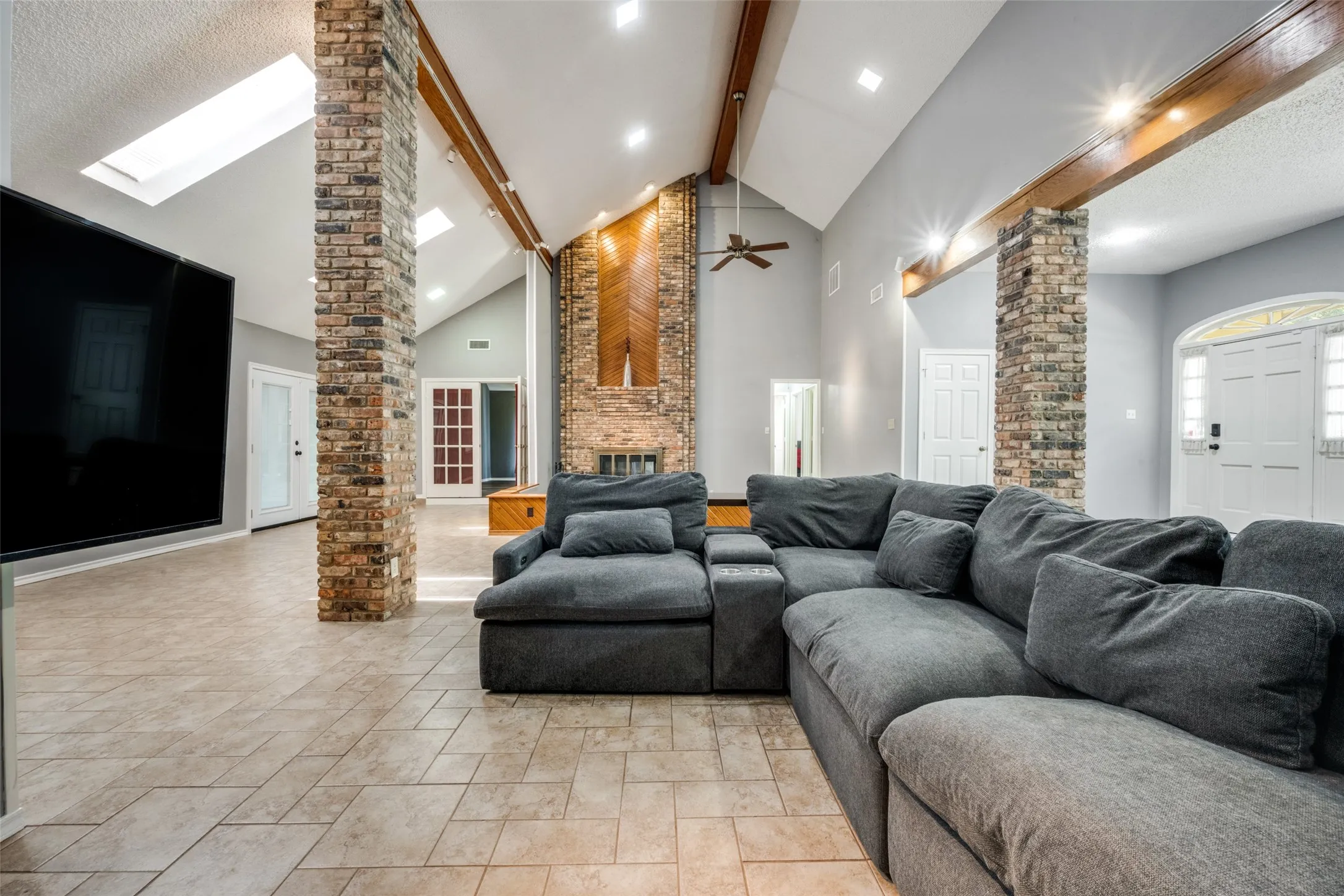 Spacious living area featuring a vaulted ceiling with skylights, exposed wood beams, and recessed lighting