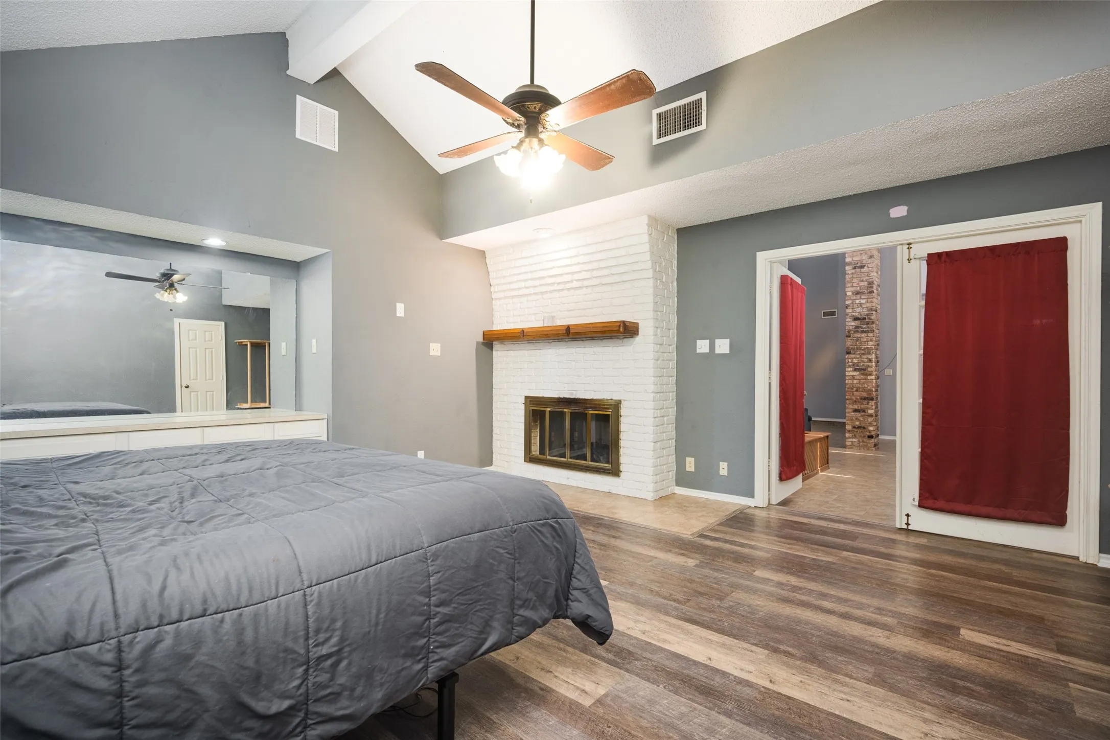 Vaulted ceiling room featuring a white painted brick fireplace with a wood mantel, wood-finish luxury vinyl plank flooring, and a ceiling fan