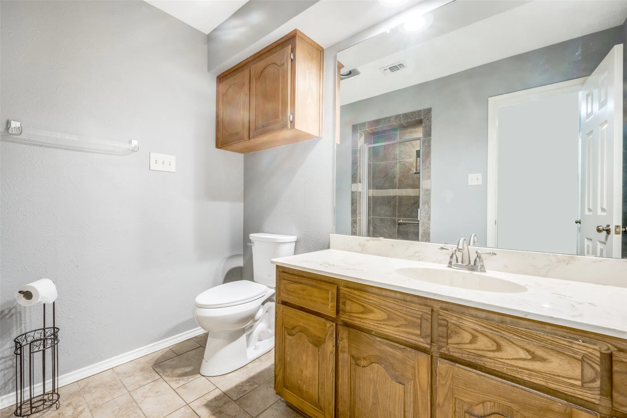 Bathroom featuring a single vanity with a white countertop and wood-finish cabinetry, a toilet, an overhead wood-finish storage cabinet, and tiled flooring