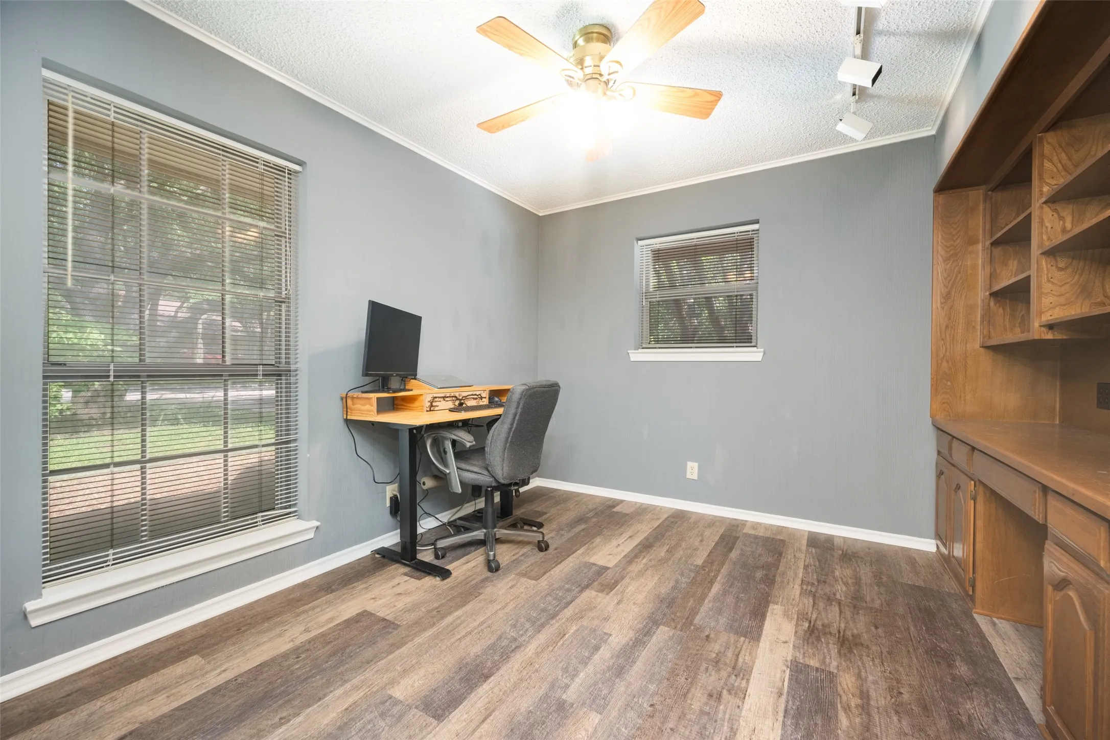 Room featuring wood finish luxury vinyl plank flooring, two windows, and a built-in wood cabinetry unit with shelves and a desk surface