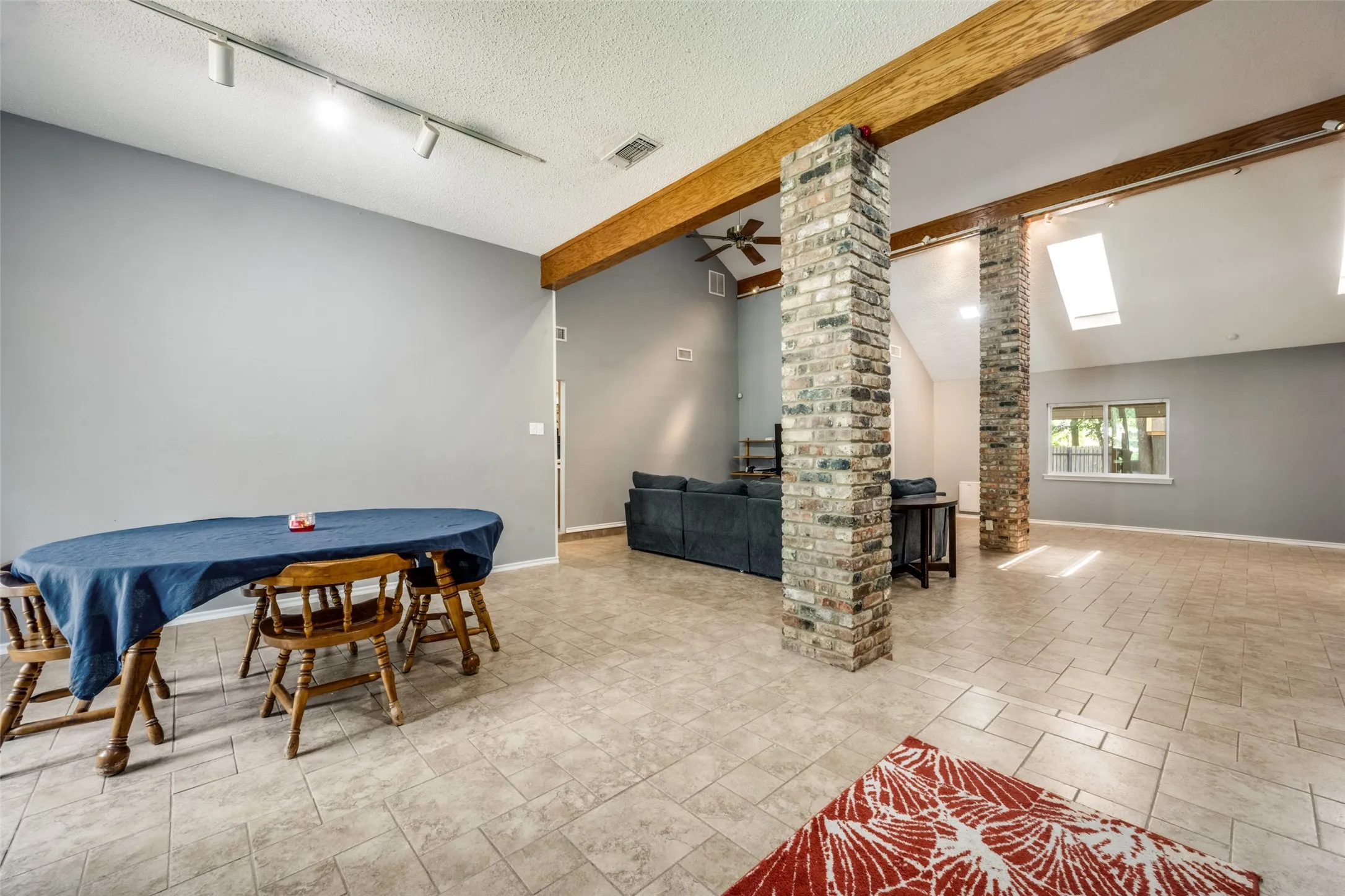 Spacious room featuring neutral tile flooring, exposed wood beams, and prominent brick columns