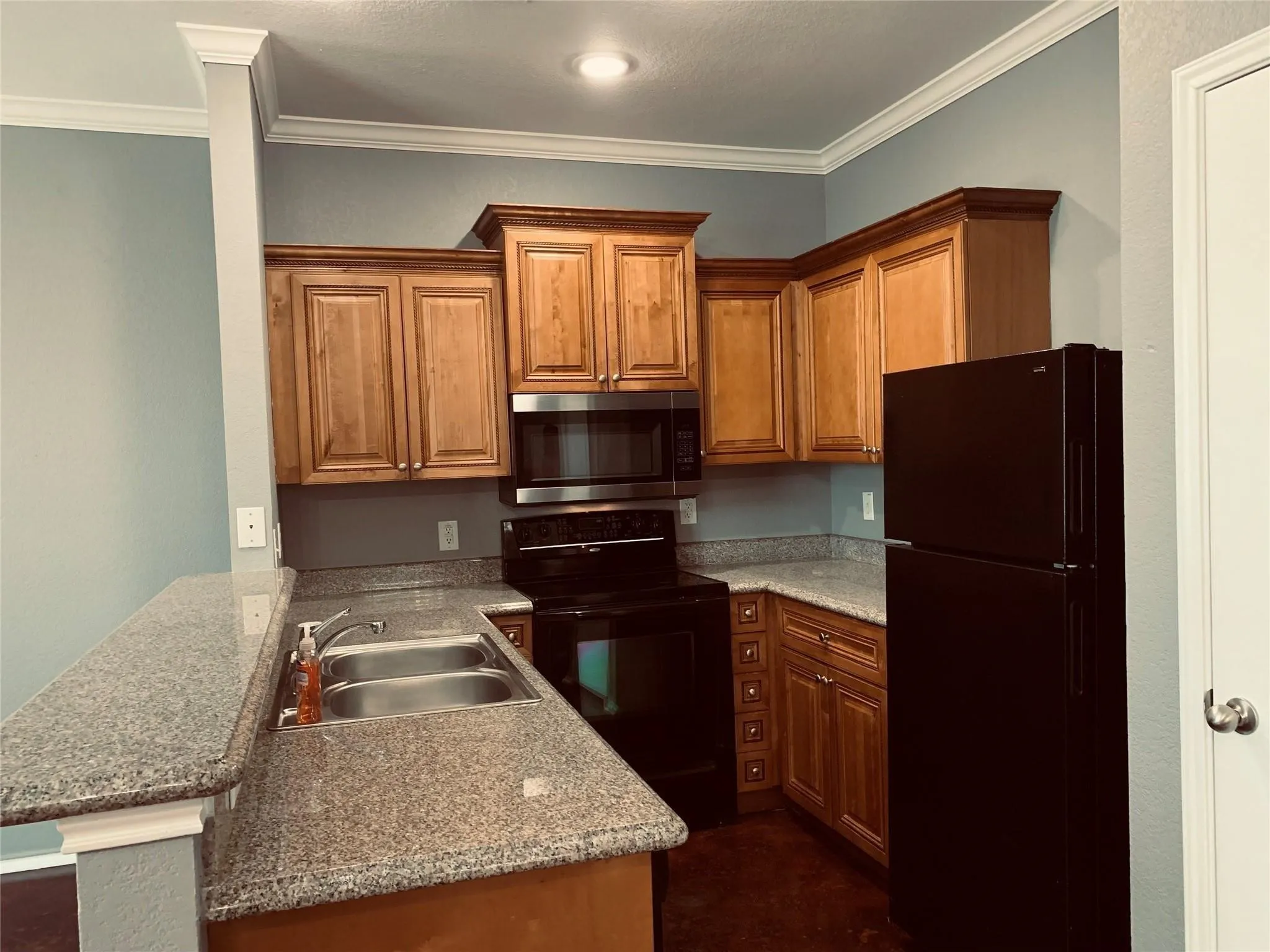 Kitchen with light stone counters, kitchen peninsula, crown molding, black appliances, and sink