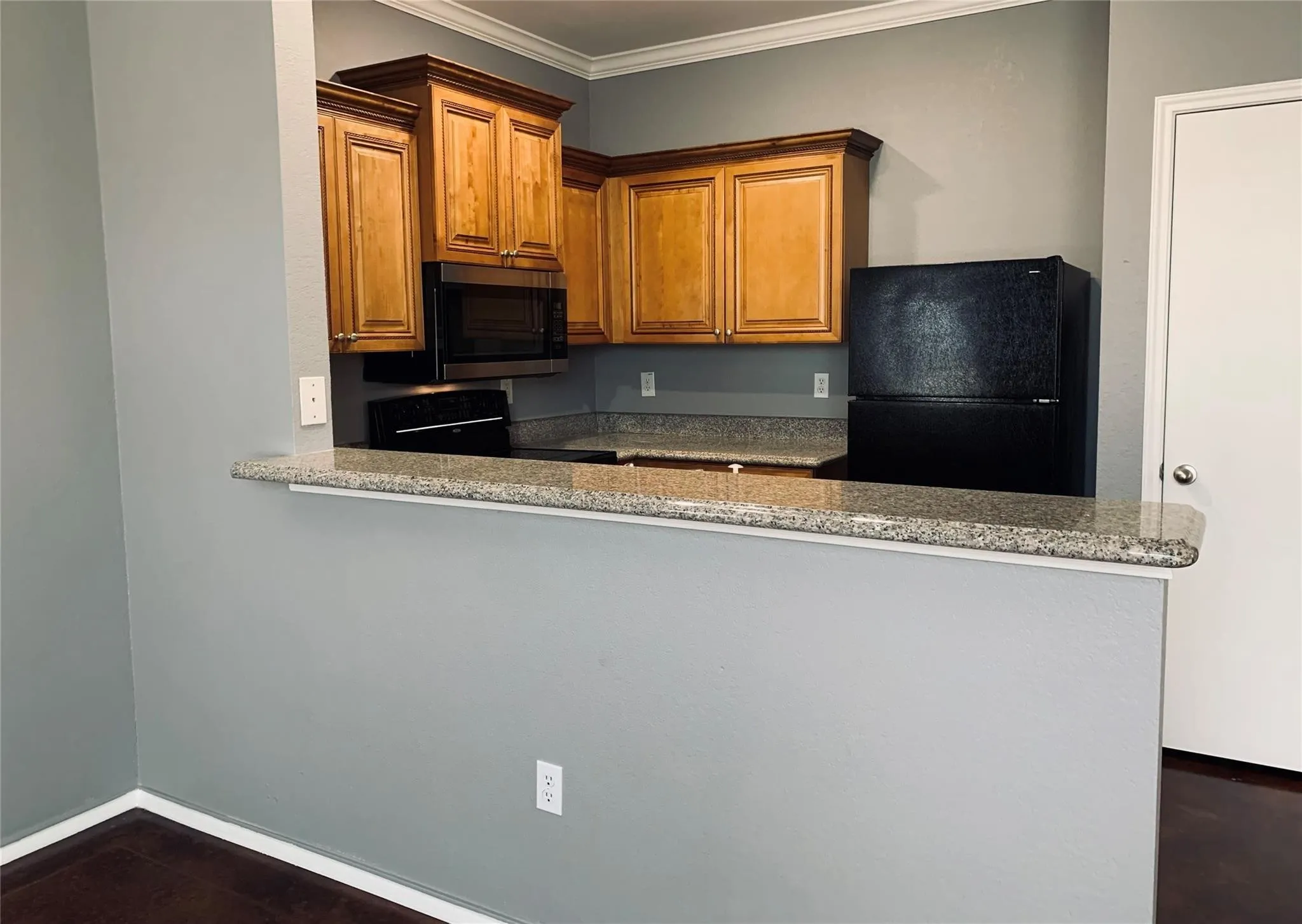 Kitchen with black refrigerator, light stone countertops, crown molding, and range