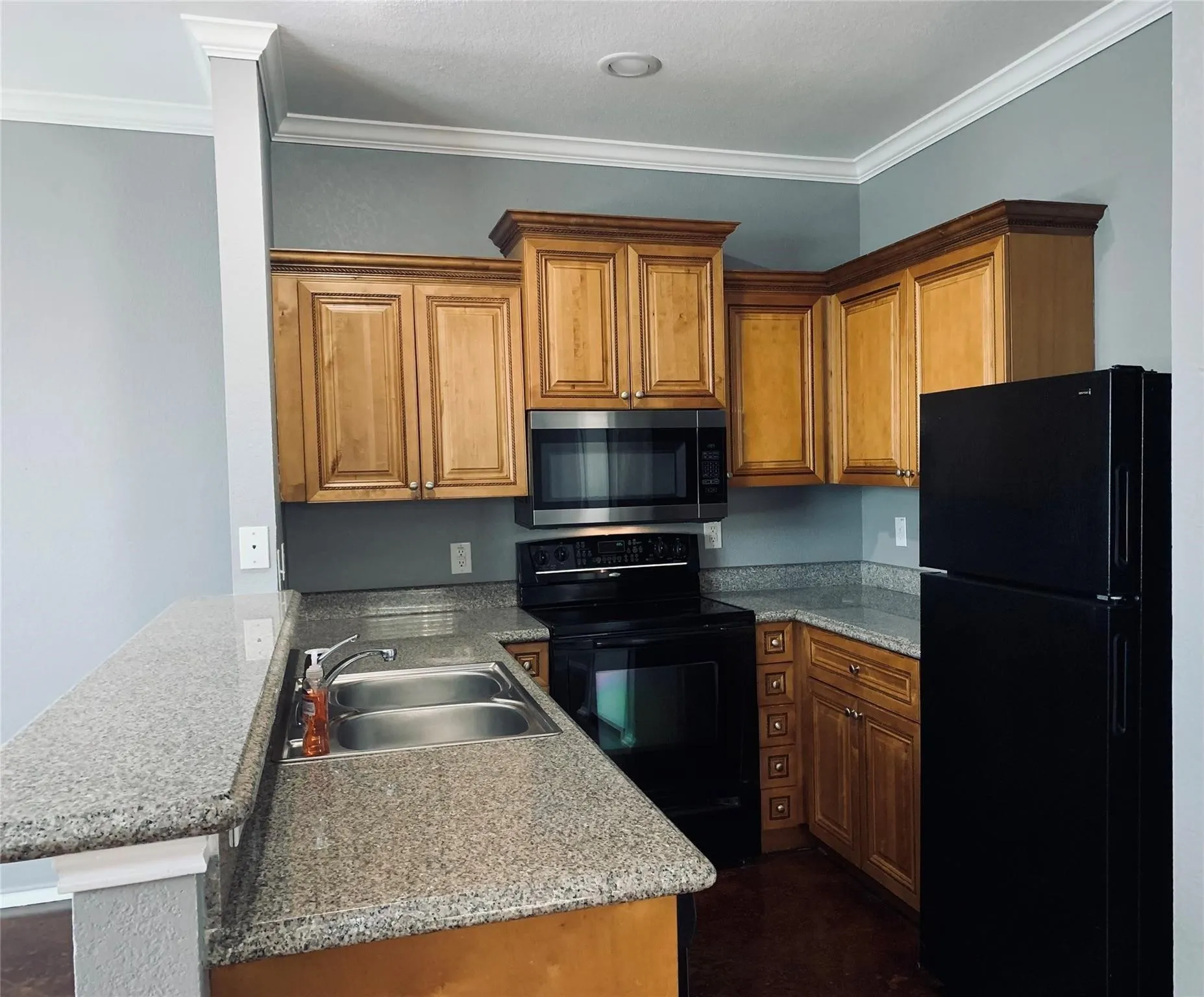 Kitchen with kitchen peninsula, black appliances, ornamental molding, light stone countertops, and sink