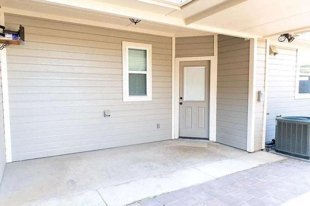 Covered patio area featuring concrete flooring, an exterior door with a window insert, and a window with blinds