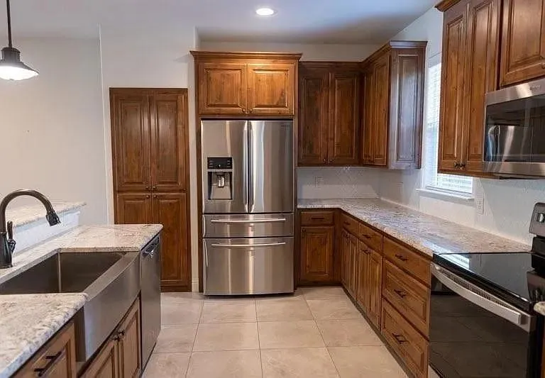 Kitchen featuring wood cabinetry, stainless steel appliances, light-toned countertops, a farmhouse-style sink, and tile flooring