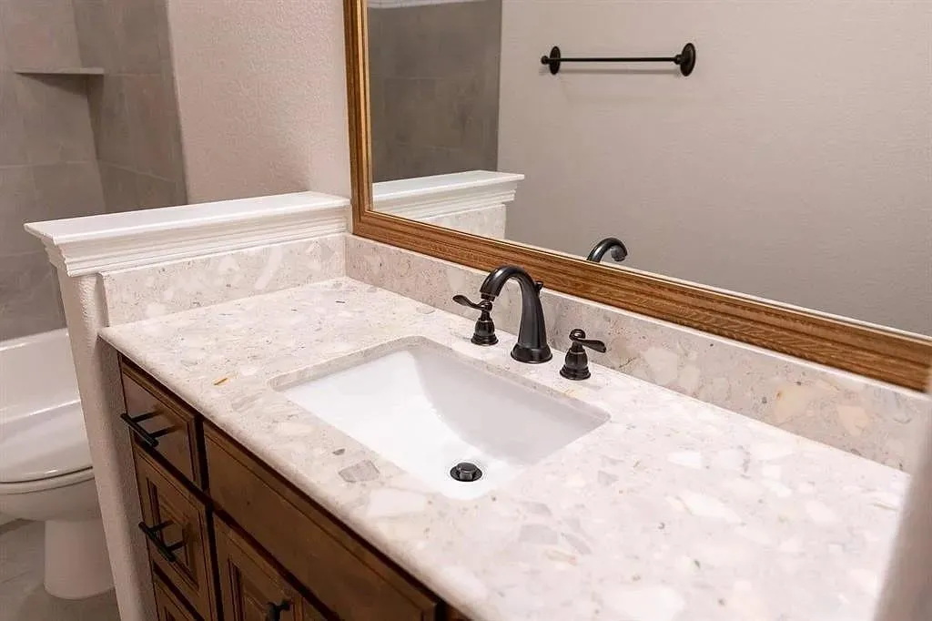 Vanity area featuring a built-in rectangular sink, light-toned countertop with integrated backsplash, and dark bronze-finish fixtures