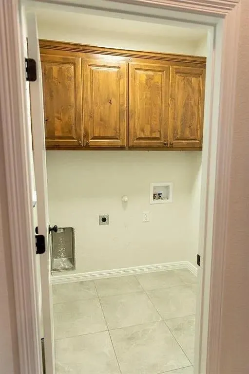 Utility room featuring upper wood cabinetry, tile flooring, and white baseboards