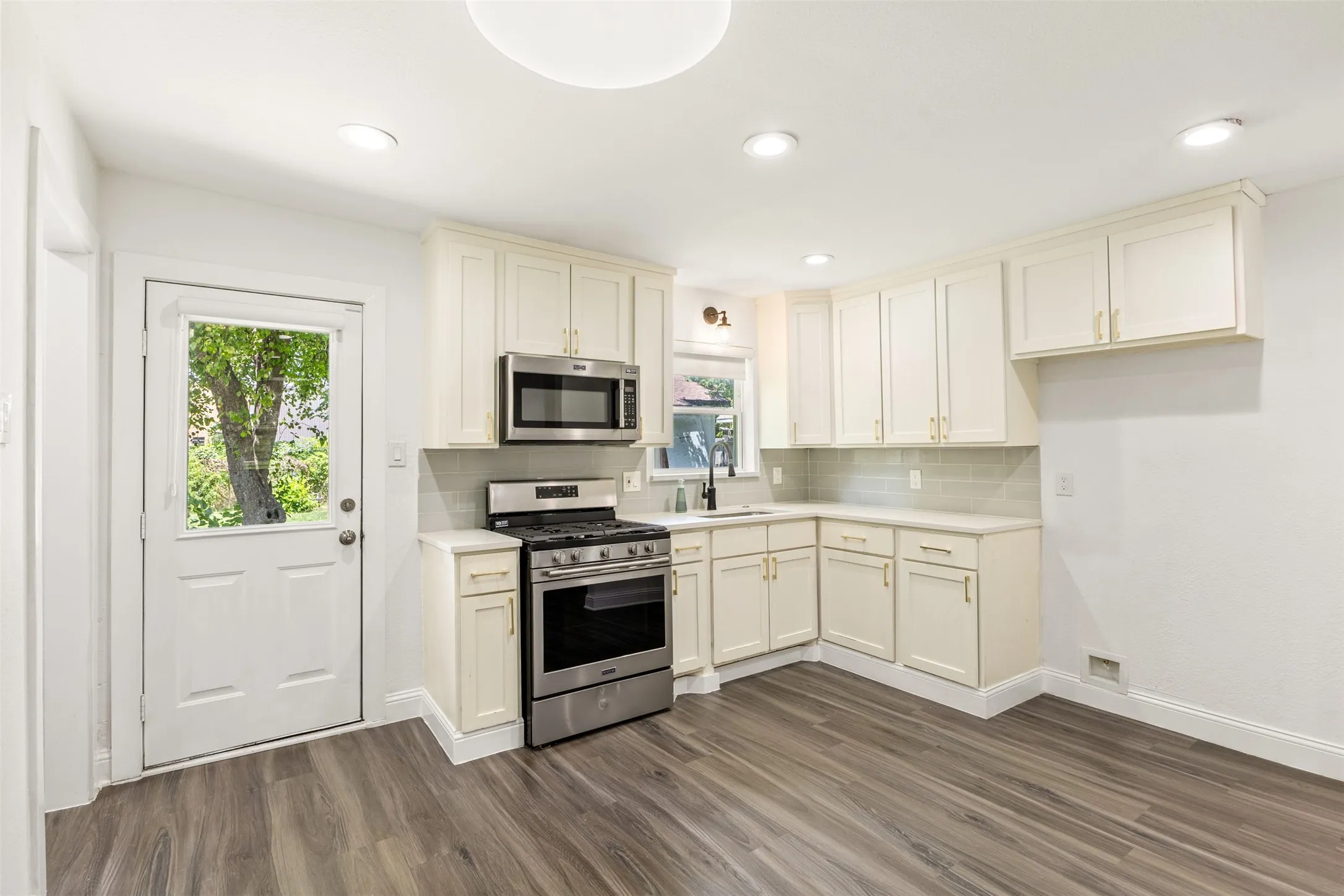 Modern kitchen featuring white cabinetry, stainless steel appliances, light countertops, and wood-finish flooring