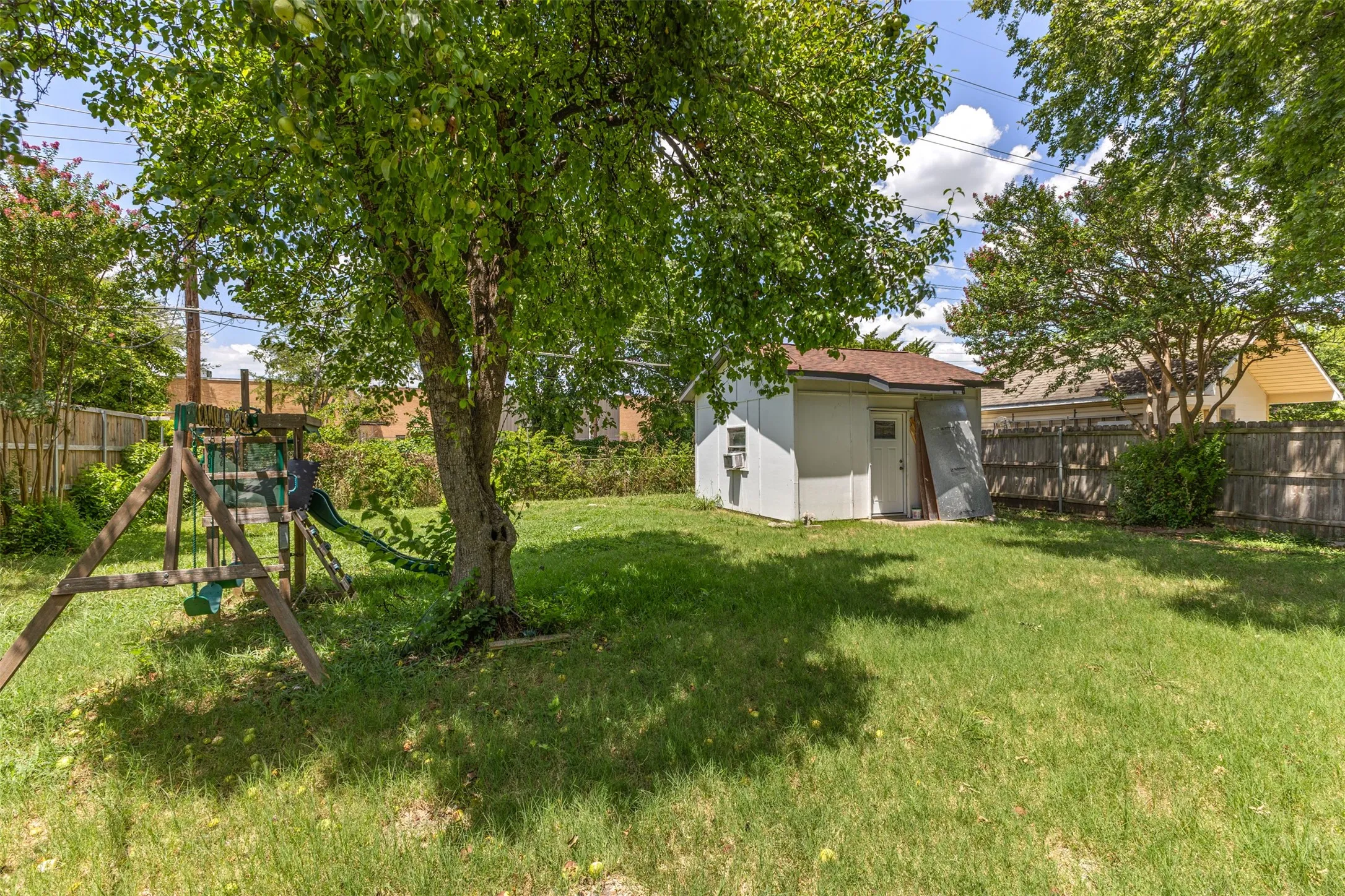Expansive backyard featuring a mature tree, privacy fencing, and a white storage shed with a brown roof