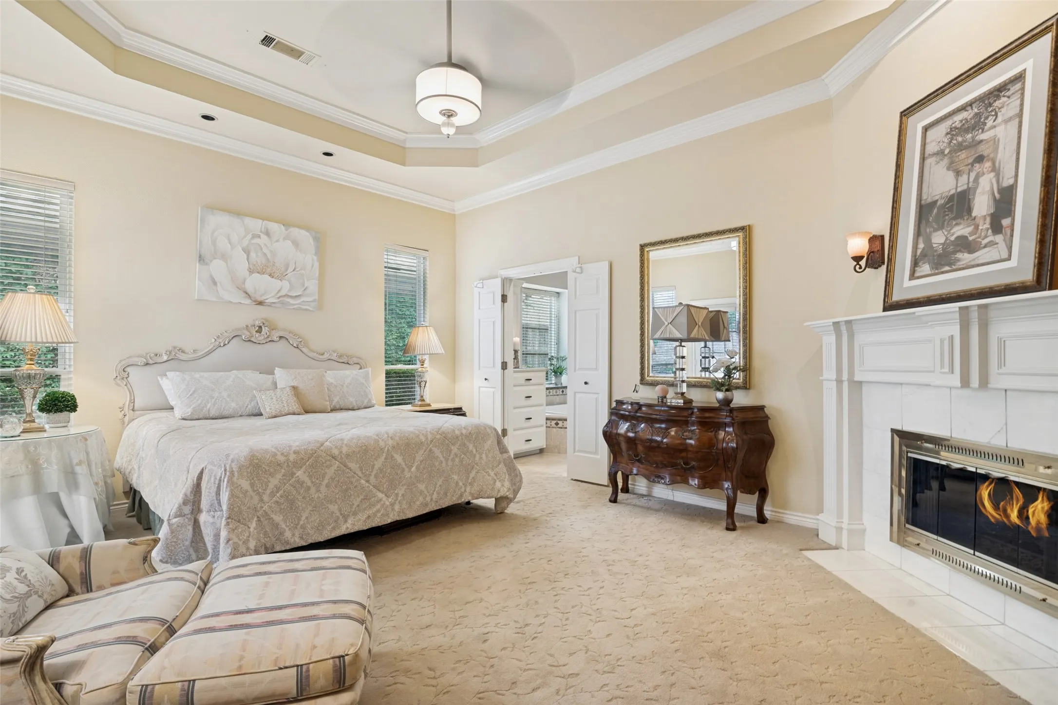 Spacious room featuring a decorative tray ceiling, crown molding, and a fireplace with a white mantel and tile surround