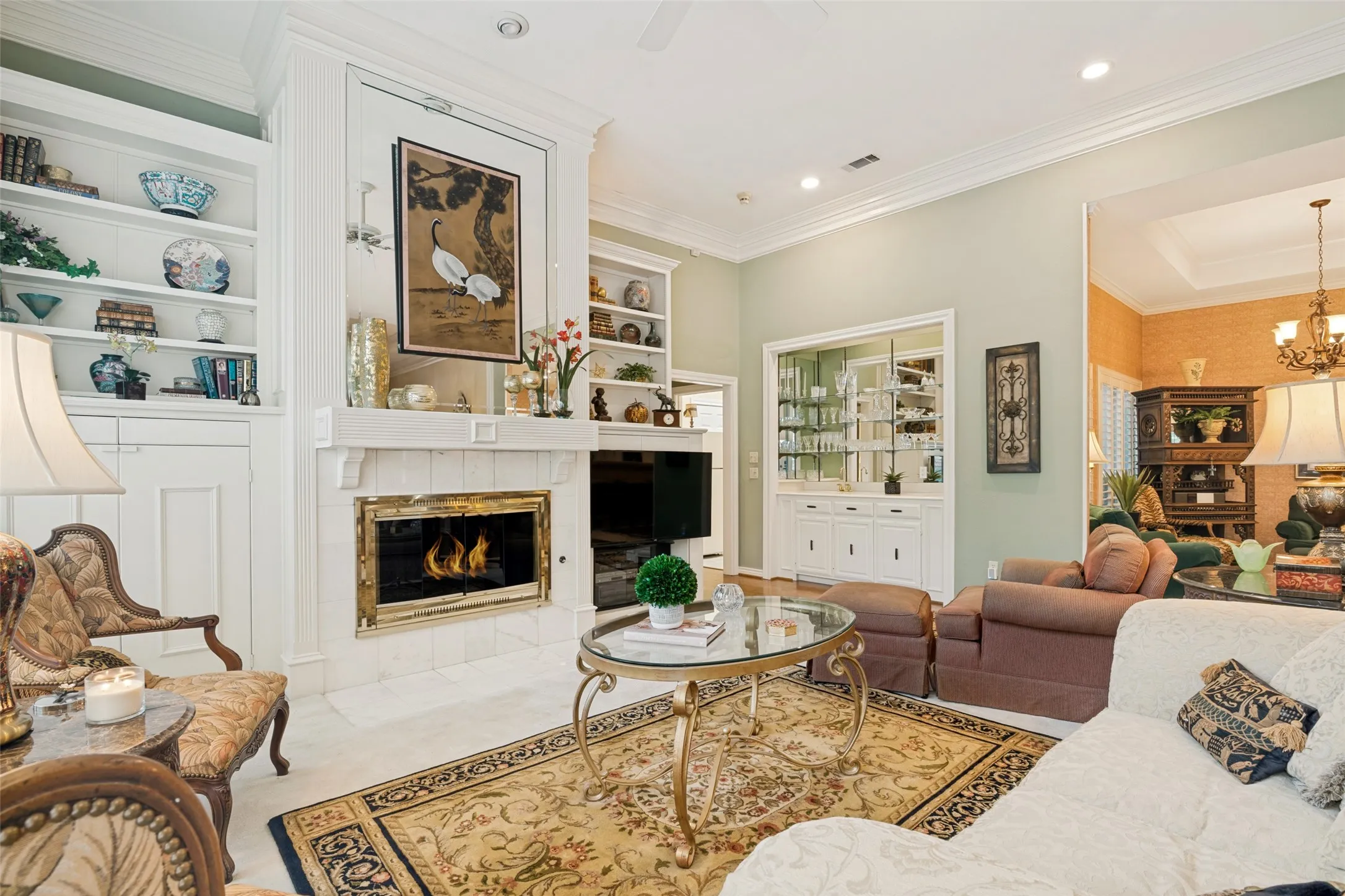Living area featuring a fireplace with a white mantel, built-in shelving, recessed lighting, crown molding, and a built-in display cabinet