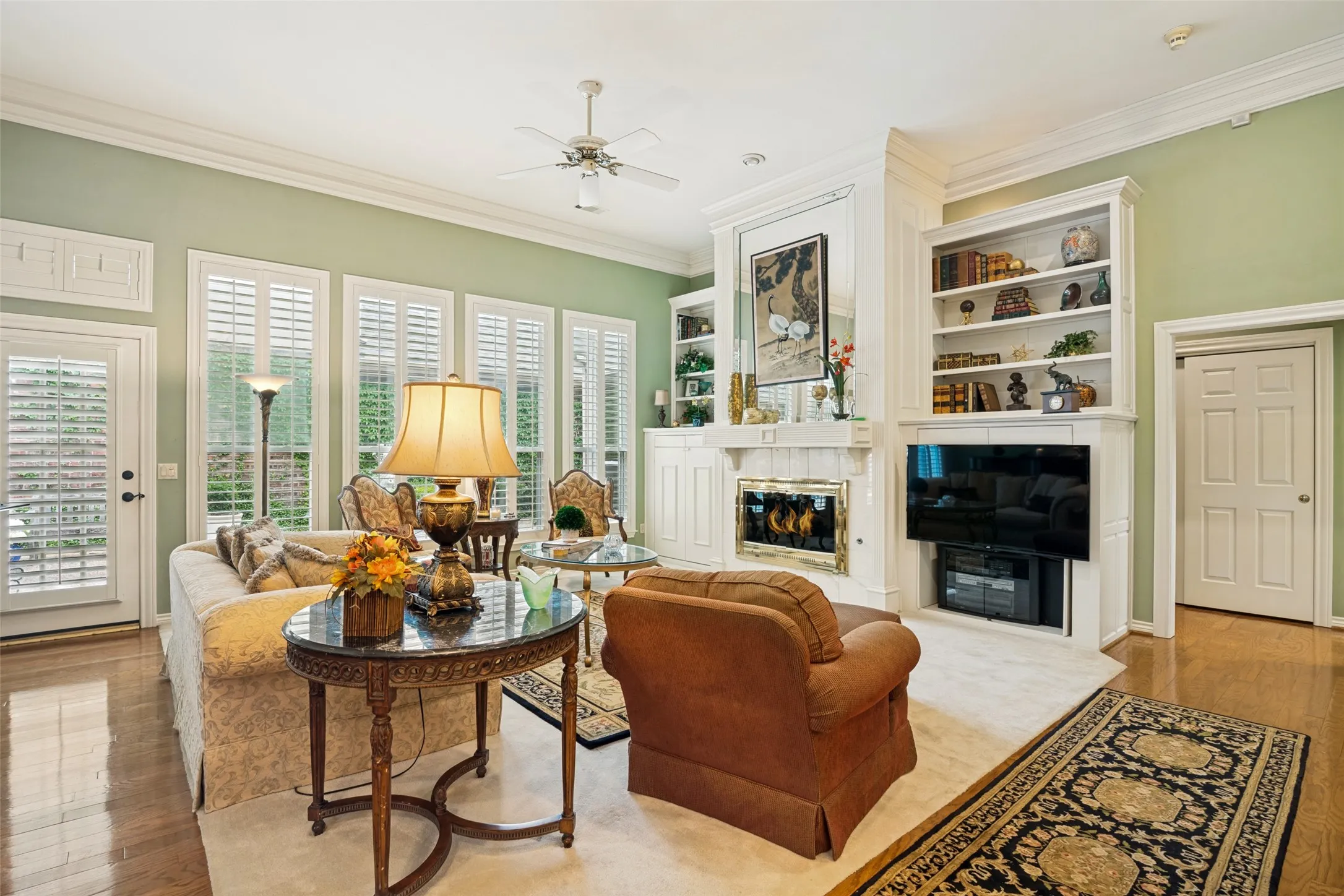 Living area featuring a fireplace, built-in shelving, rich wood-finish flooring, and multiple windows with plantation shutters