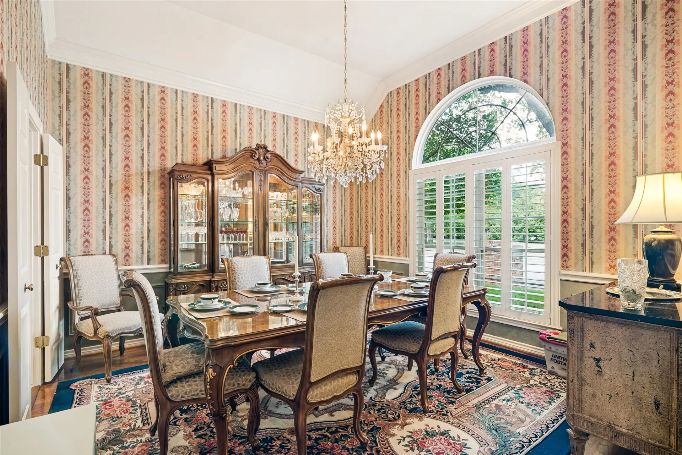 Formal dining room featuring a large arched window with plantation shutters, a crystal chandelier, and crown molding