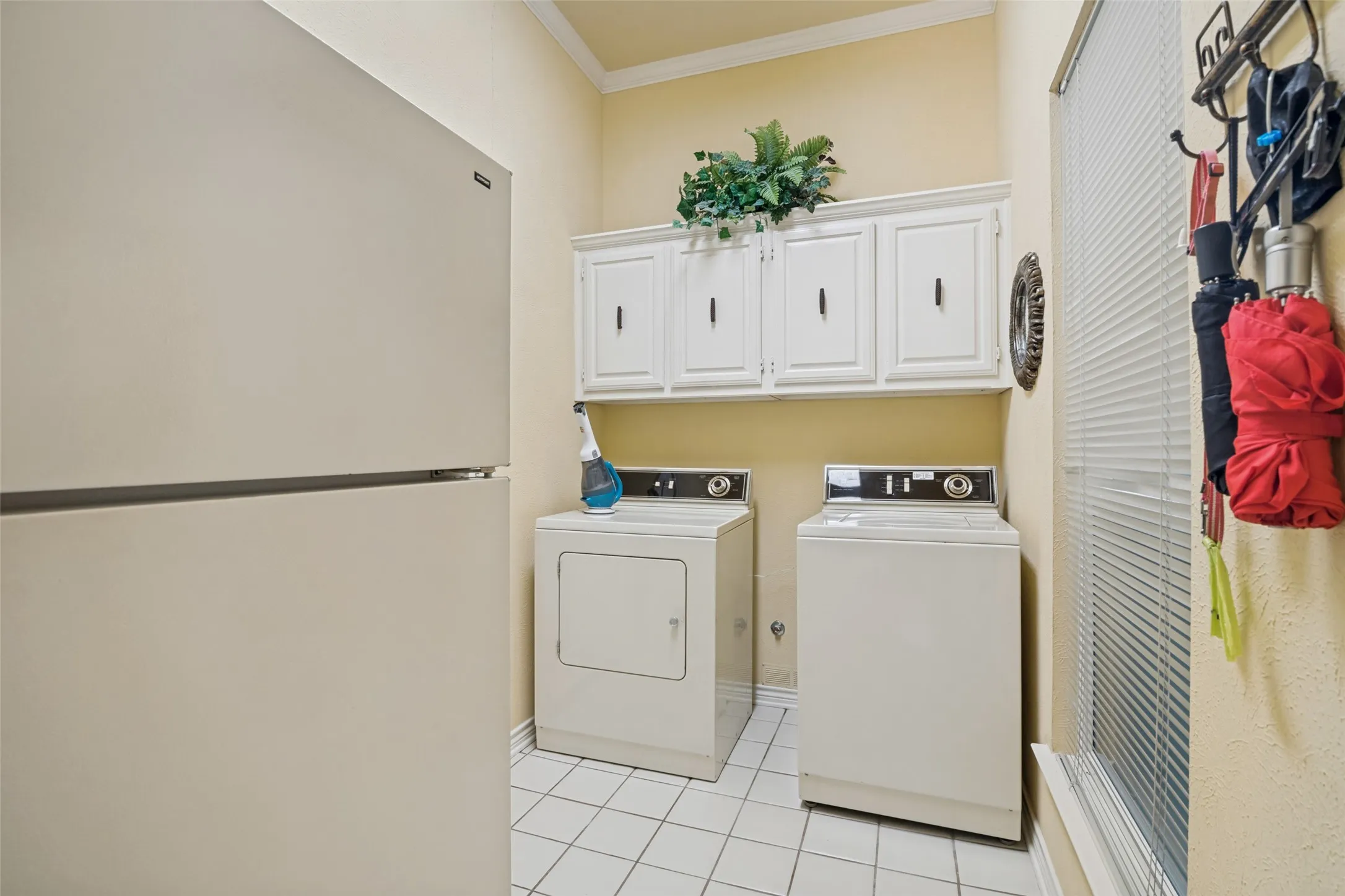 Dedicated utility area featuring white upper cabinetry, tiled flooring, and a window with blinds