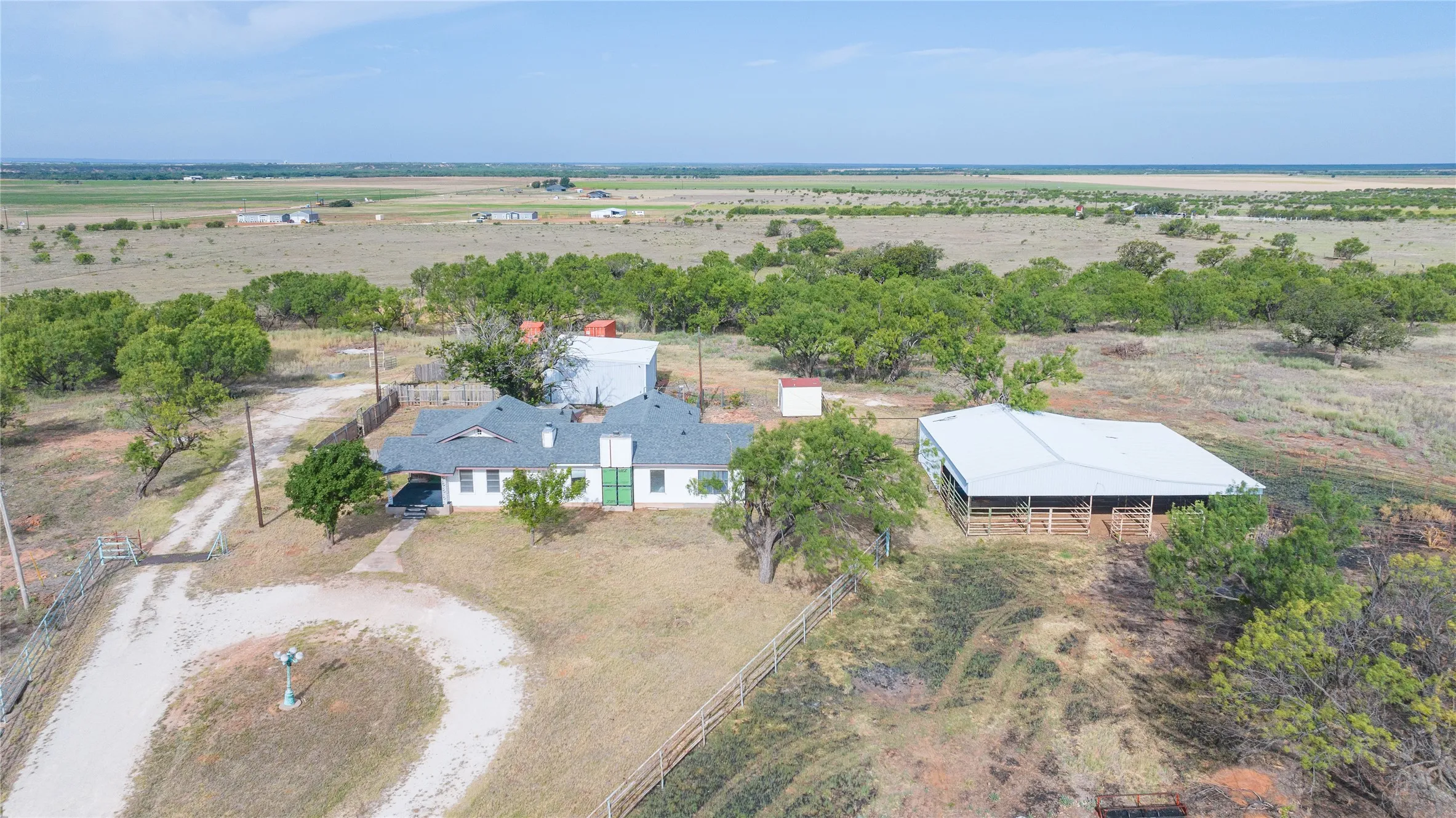 Expansive property featuring a white ranch-style residence, a large metal-roofed barn, and a gravel driveway